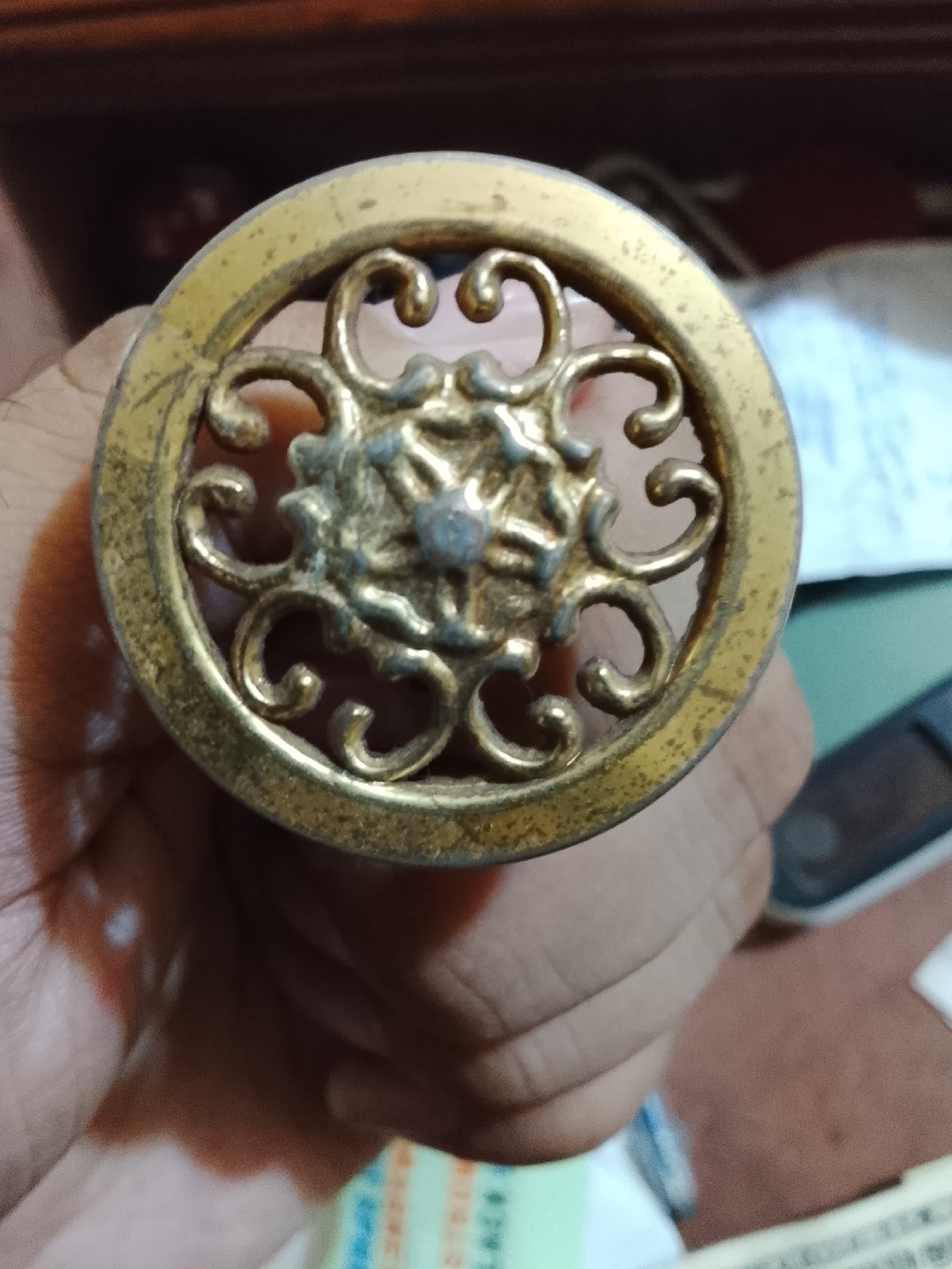 A person's hand holds a round, decorative object with an intricate, floral-like design cut out of a gold-colored metal. The object appears to be slightly tarnished or aged. It's difficult to determine the exact location or details without more information beyond what is shown in the image. There's nothing in the image to indicate it is from Multan, Pakistan.