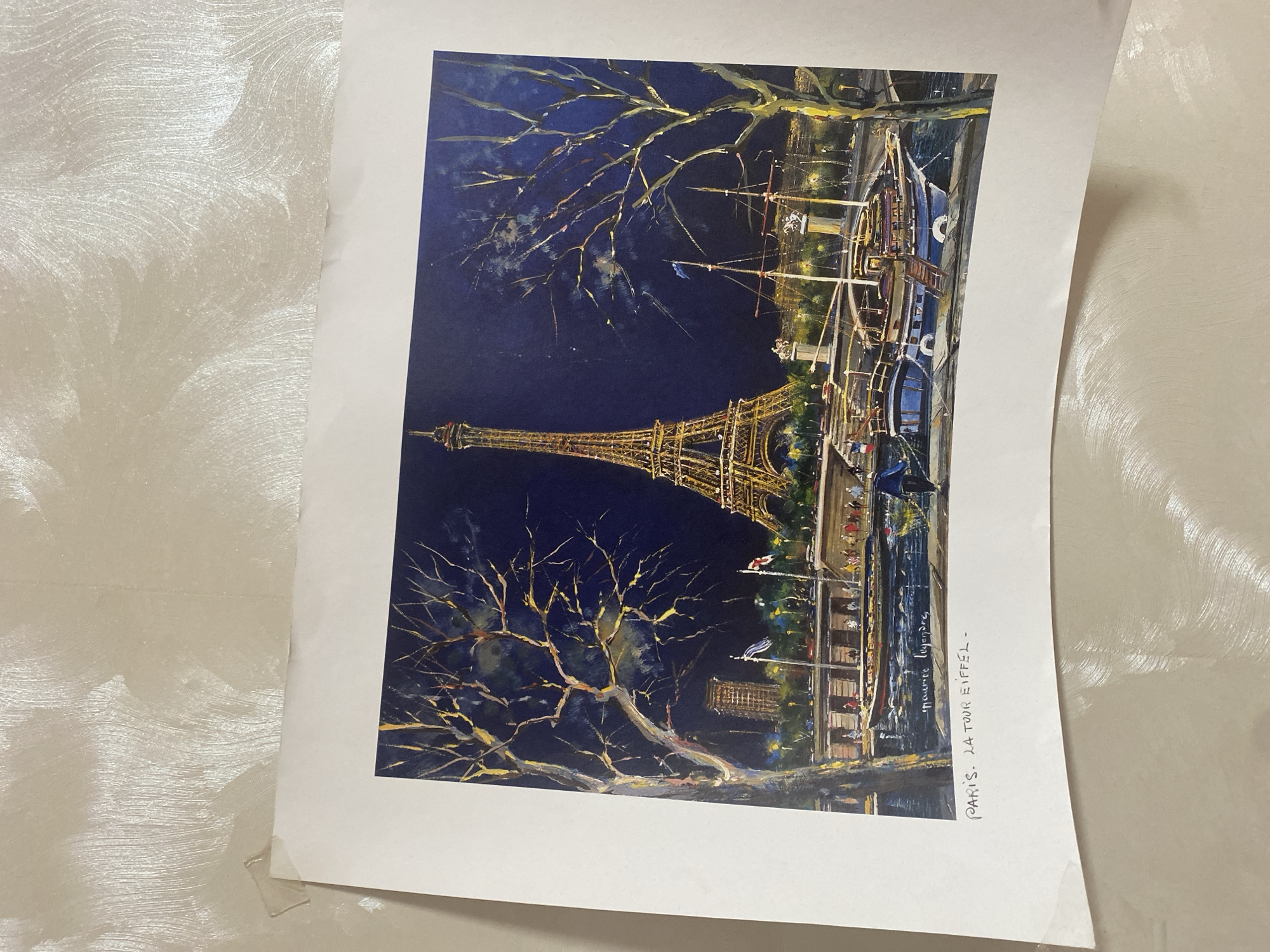 The image is a painting of the Eiffel Tower at night. The tower is illuminated, and the surrounding buildings and trees are also lit. There is a body of water in the foreground with several boats. The painting is signed by "Maurice Legendre" and has the title "PARIS. LA TOUR EIFFEL." There is no information in the image that suggests a connection to Chornomorsk, Ukraine.