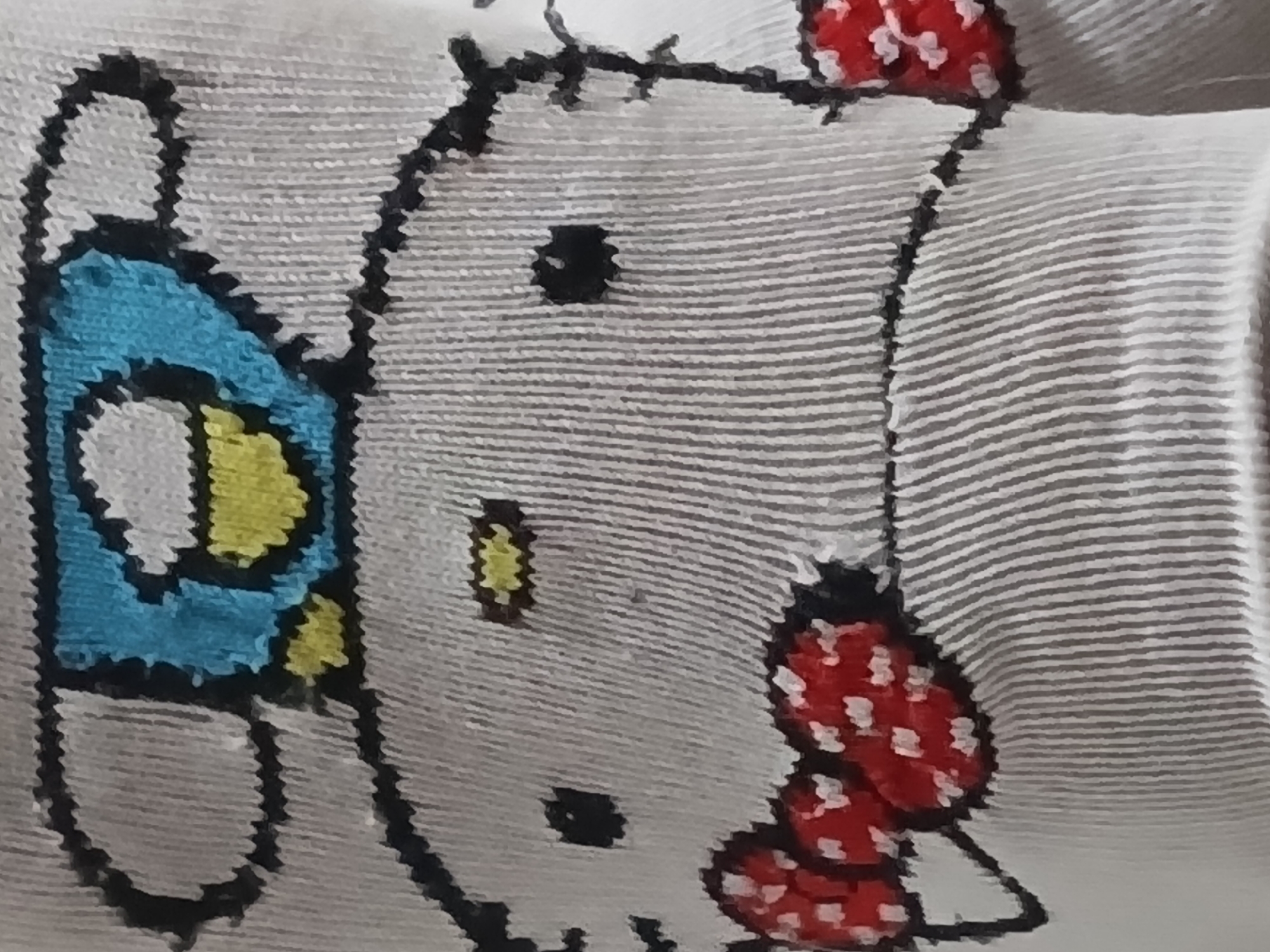 A close-up of fabric depicting the cartoon character Hello Kitty with a mask and bow. The fabric has a horizontal striped pattern. The mask is blue and yellow, and the bow is red with white spots. The scene does not depict a location, interaction, or environment beyond the fabric itself. The image does not provide information to determine if this scene is in Buenos Aires, Argentina.