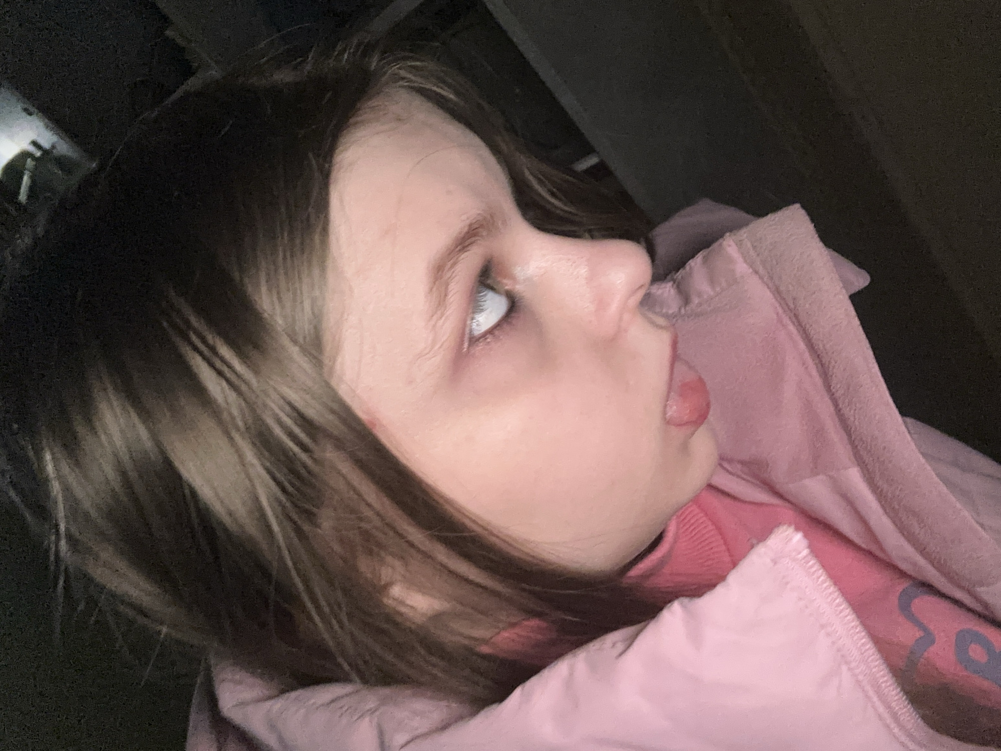 A girl with brown hair and fair skin is visible. She is wearing a pink jacket and a pink sweater. The background is dark and indistinct. There is no indication of the location being Moscow, Russia.