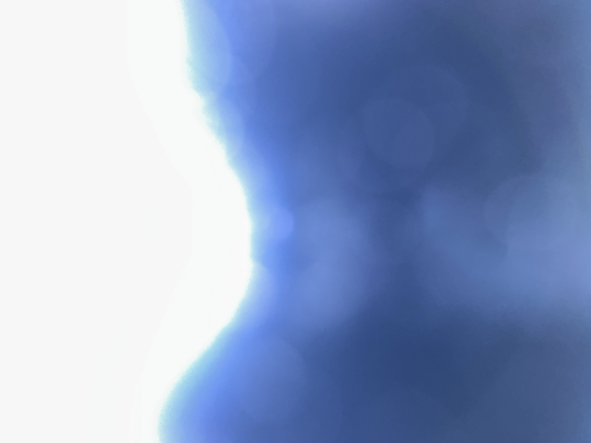 The image displays an abstract, out-of-focus view of a bright, white light bleeding into a gradient of blues. The top portion of the image is dominated by a stark white, suggesting a strong light source or the sky. Below this, the white transitions into a lighter blue, which then deepens into a darker, richer blue, occupying the majority of the lower frame. There are soft, circular blurs of light scattered within the blue areas, possibly representing bokeh effects from the camera lens or reflections. The overall impression is one of light and color rather than a recognizable scene. The image does not contain any discernible elements that would allow for identification of a specific location in Belgrade, Serbia.
