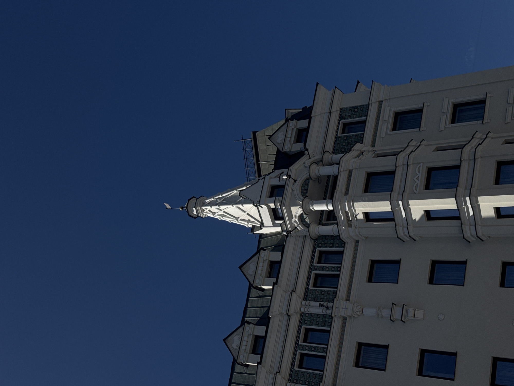 The image shows a low-angle view of the Radisson Collection Hotel, Moscow. The architecture is a Soviet-era neoclassical style with a prominent spire. The sky is clear and blue, suggesting sunny weather. No people are visible in the frame.