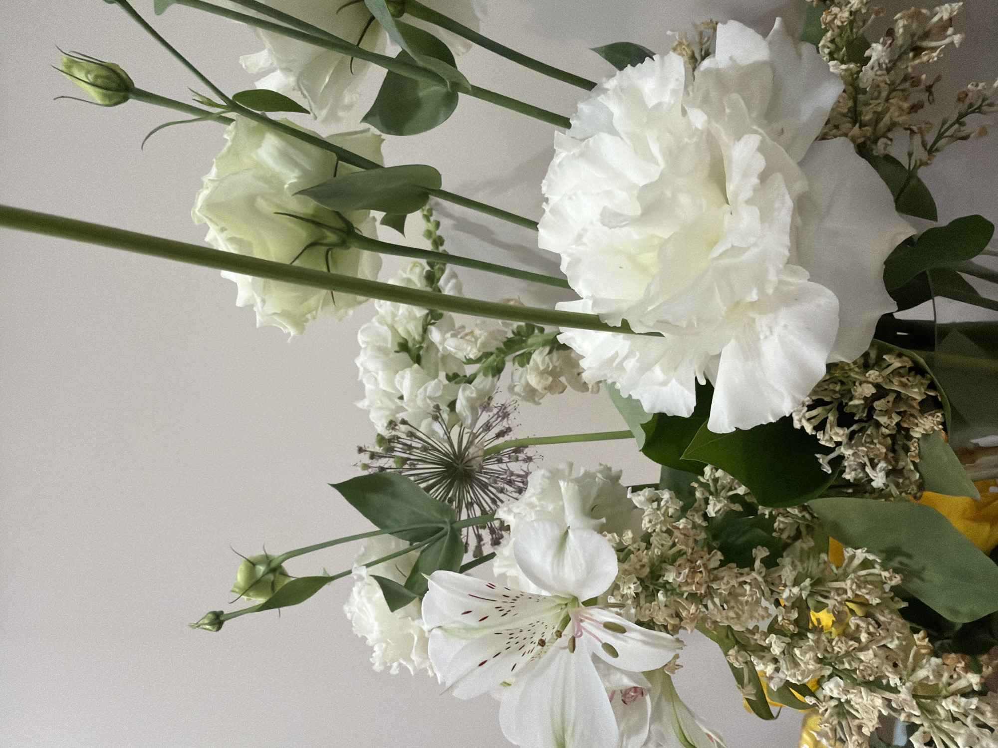 A close-up of a bouquet of predominantly white flowers against a pale background. The flowers include white lisianthus, alstroemeria with maroon spots, and delicate dried flowers. Green stems and leaves are visible. The location in Yerevan, Armenia, is not discernible from the image alone.