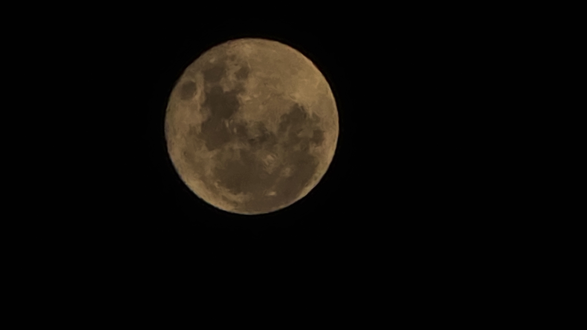A full, bright moon dominates the upper left quadrant of a black sky. The moon's surface details are visible, with varying shades of brown and gray indicating craters and lunar features. The rest of the image is dark and devoid of any other visible objects or details. The scene is not identifiable as being in the city of Saint Petersburg, Russia.