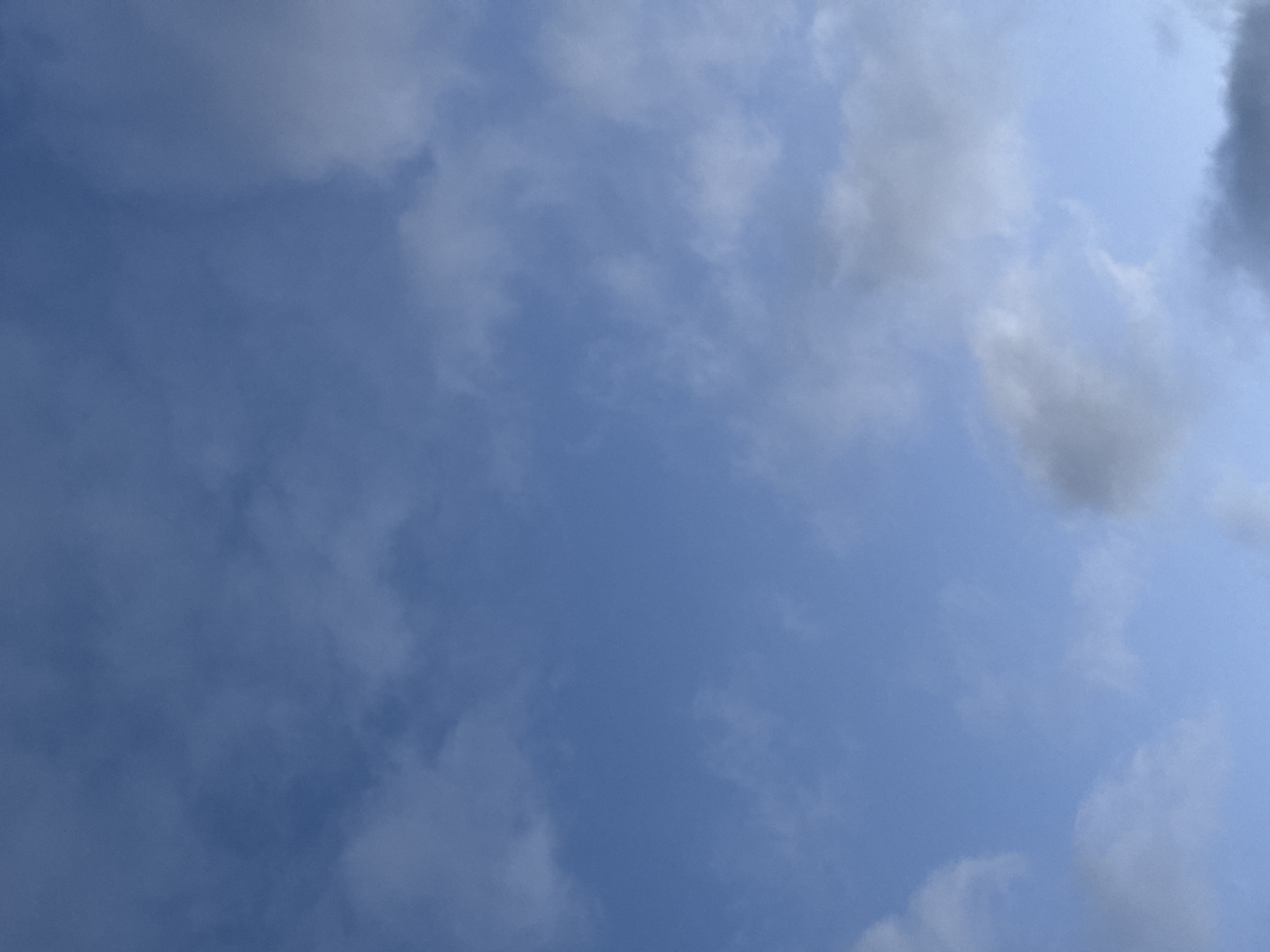 The image shows a clear blue sky with scattered white and gray clouds. The clouds are wispy and appear to be moving, suggesting a breezy day. There are no people or objects visible in the image, and the focus is entirely on the sky. The scene is natural and serene. It's impossible to determine the location within Santiago de Compostela based solely on this image, as it depicts a generic sky.