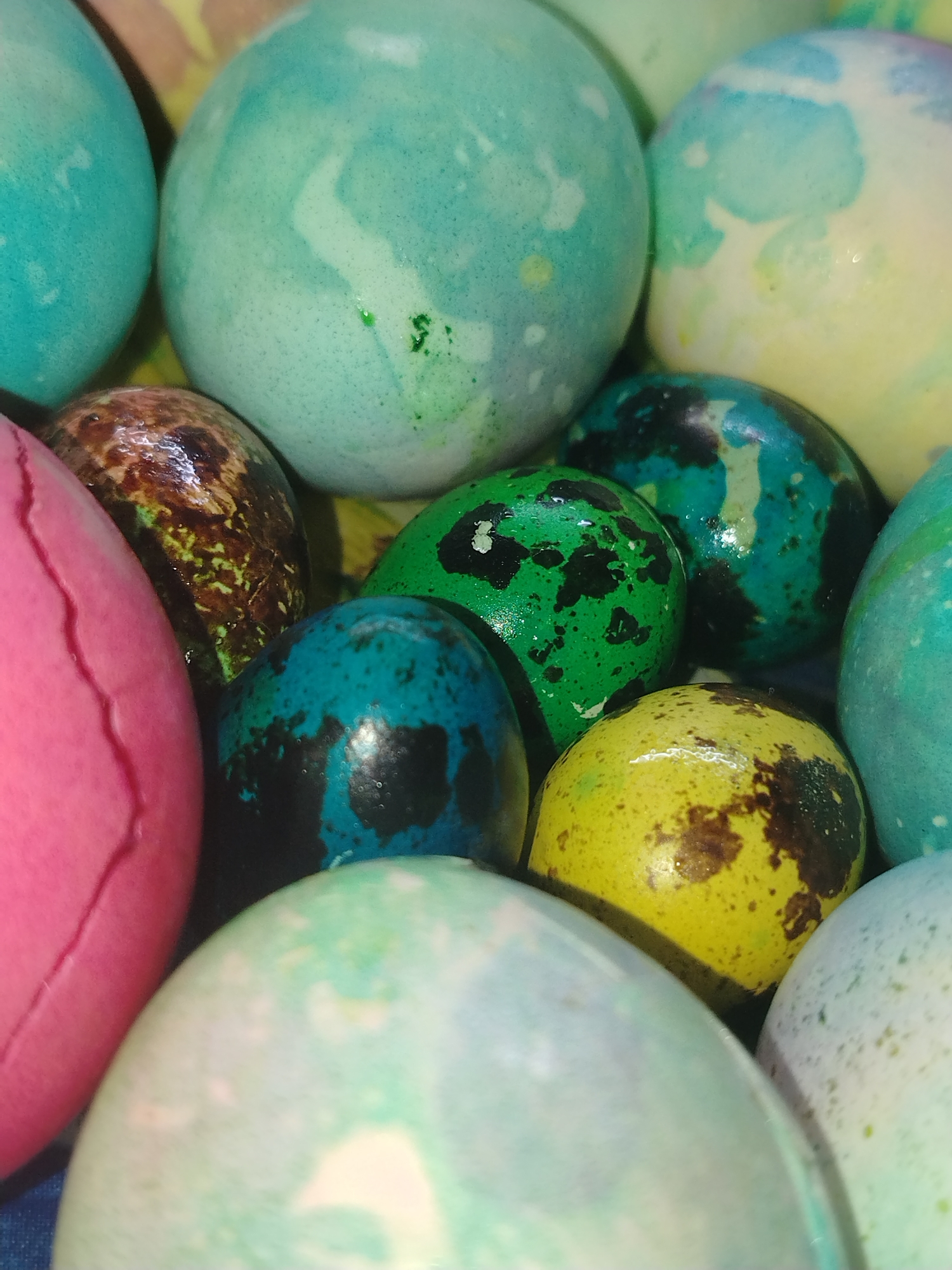 The image shows a collection of dyed eggs in various colors and patterns. Colors include blue, green, pink, yellow, and brown with marbled, speckled, and solid patterns. The eggs are clustered together, obscuring any background details. There is no indication of the location being Noviy, Russia, nor is there any evidence of people, actions, or interactions.