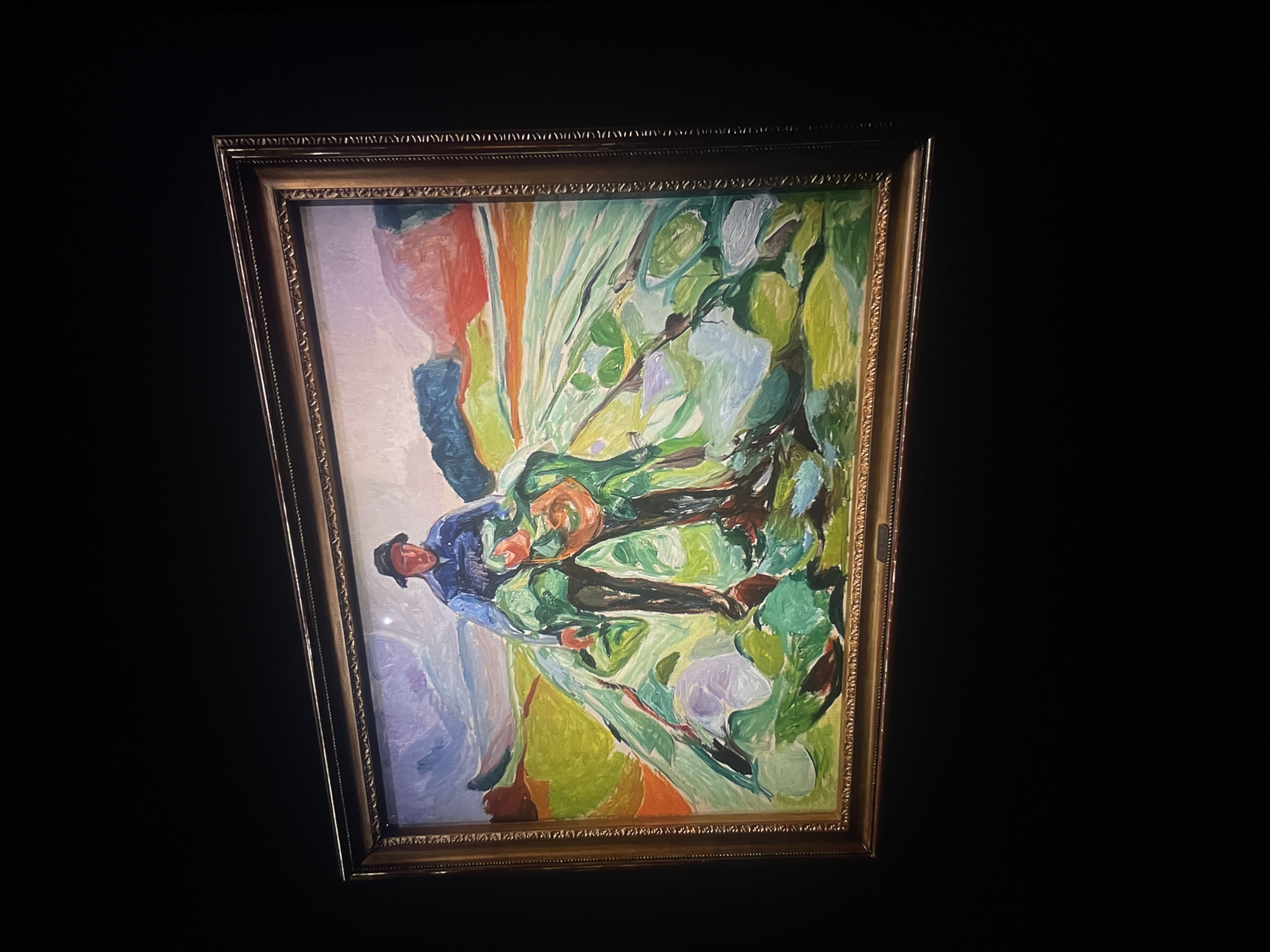 A framed painting hangs against a dark background. The painting depicts a man with a hat, rendered in an impressionistic style with broad brushstrokes of blue, green, orange, and white. The location is not specified.