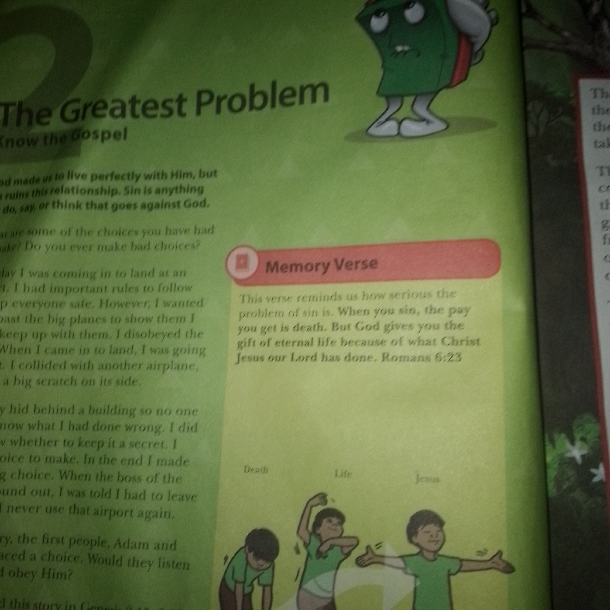 The image is a close-up, eye-level shot of an open book, predominantly featuring text and illustrations against a green background. The title of the page is "The Greatest Problem" followed by "Know the Gospel". A section labeled "Memory Verse" contains a verse from Romans 6:23. Below the text, there are three cartoon-style illustrations of children, labeled "Death", "Life", and "Jesus". To the right of the main content, a portion of another page is visible, with a black background and faint green foliage, containing some text that appears to be related to the book's content. The book is open and flat, with the pages slightly curved. The lighting is uneven, creating some glare and shadows, particularly on the right side of the image. The image does not contain any information about a specific city or location.