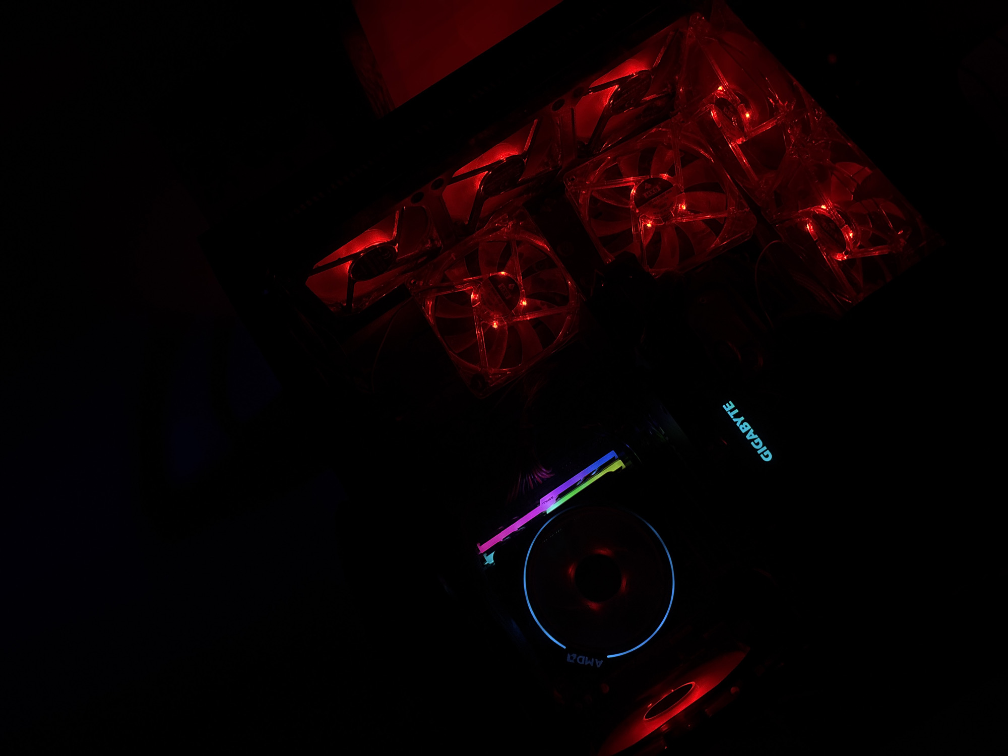 The image shows the interior of a computer. There are multiple red-lit case fans arranged in the upper portion of the frame. In the lower right, there is a Gigabyte branded component, likely a graphics card, with a blue-lit fan and some multi-colored lighting elements. Another red-lit fan is partially visible in the very bottom center. The scene is dimly lit. It is not possible to determine if the image was taken in Durmersheim, Germany.