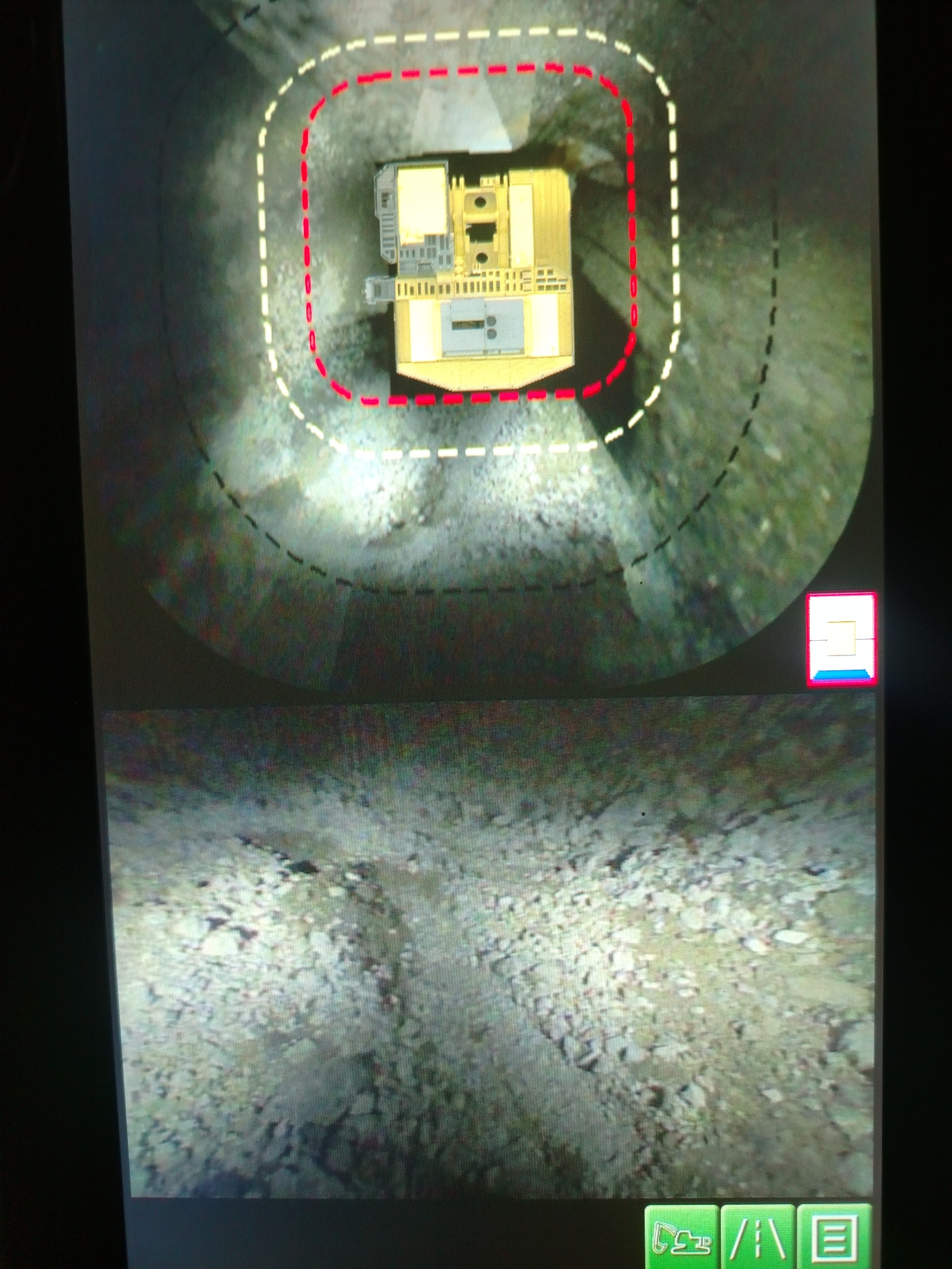 The image displays a split screen. The top portion shows a bird's-eye view of a construction vehicle, possibly a backhoe, within a circular path marked by dashed red and white lines on a gravelly surface. The vehicle is yellow and gray. A small, stylized icon is in the bottom right corner. The bottom portion of the screen shows a ground-level view of a rocky, uneven terrain, likely a construction site. In the bottom right corner of this lower section are three green icons, one resembling a bulldozer, another a road, and the third a document. The scene is not identifiable as being in Naminga, Russia.