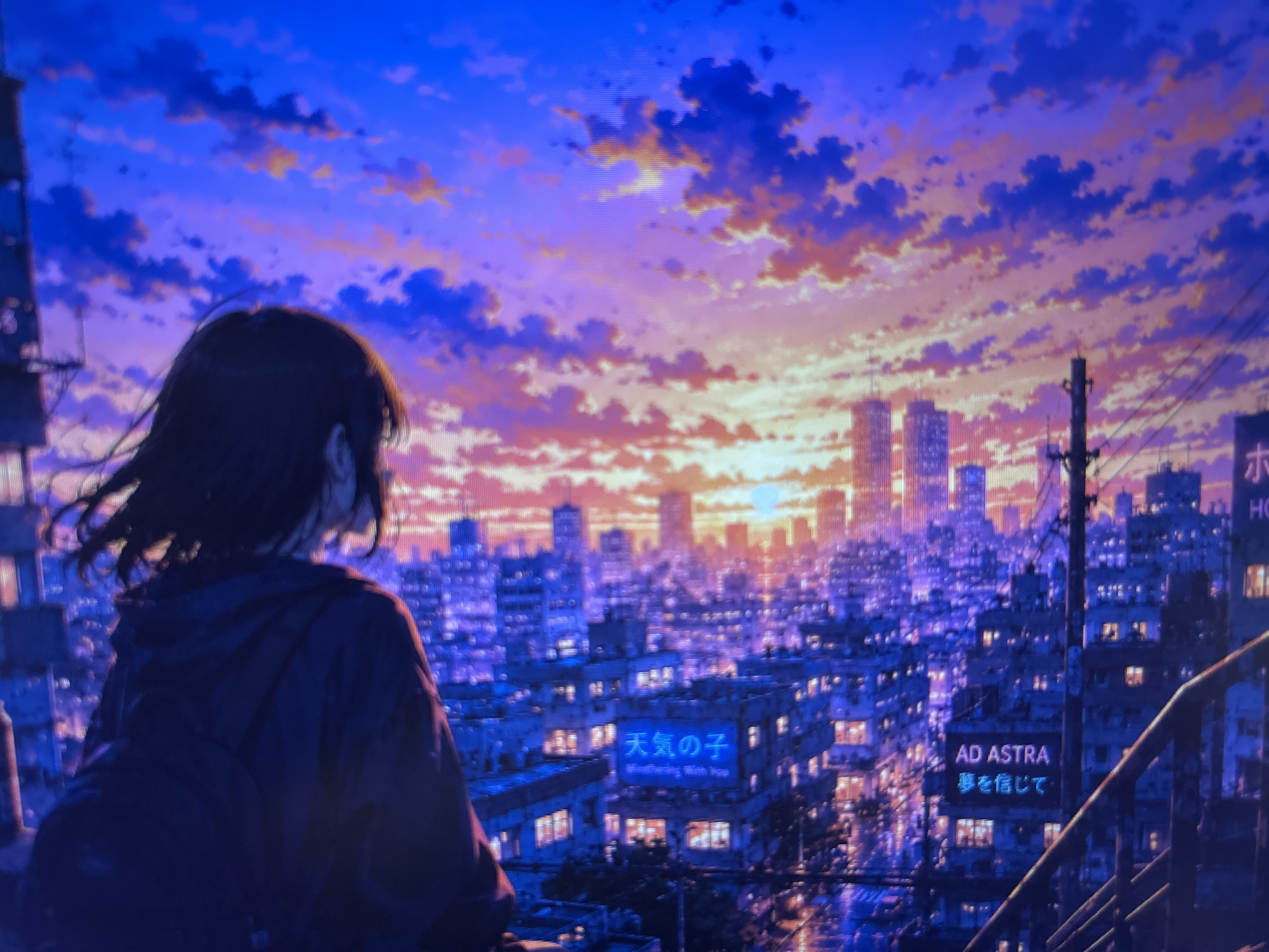 The image depicts a stylized scene of a cityscape at sunset. In the foreground, a figure with short, dark hair and a backpack stands with their back to the viewer, gazing out at the city. The skyline is filled with densely packed buildings, illuminated by the setting sun. The sky is a mix of purple, blue, and orange hues, with clouds scattered throughout. Signs with Japanese text, including one that says "Weathering With You" and "AD ASTRA", are visible on some of the buildings. A telephone pole and some railings are visible on the right side of the image. The overall tone of the image is evocative and atmospheric. The location is not Sofia, Bulgaria.