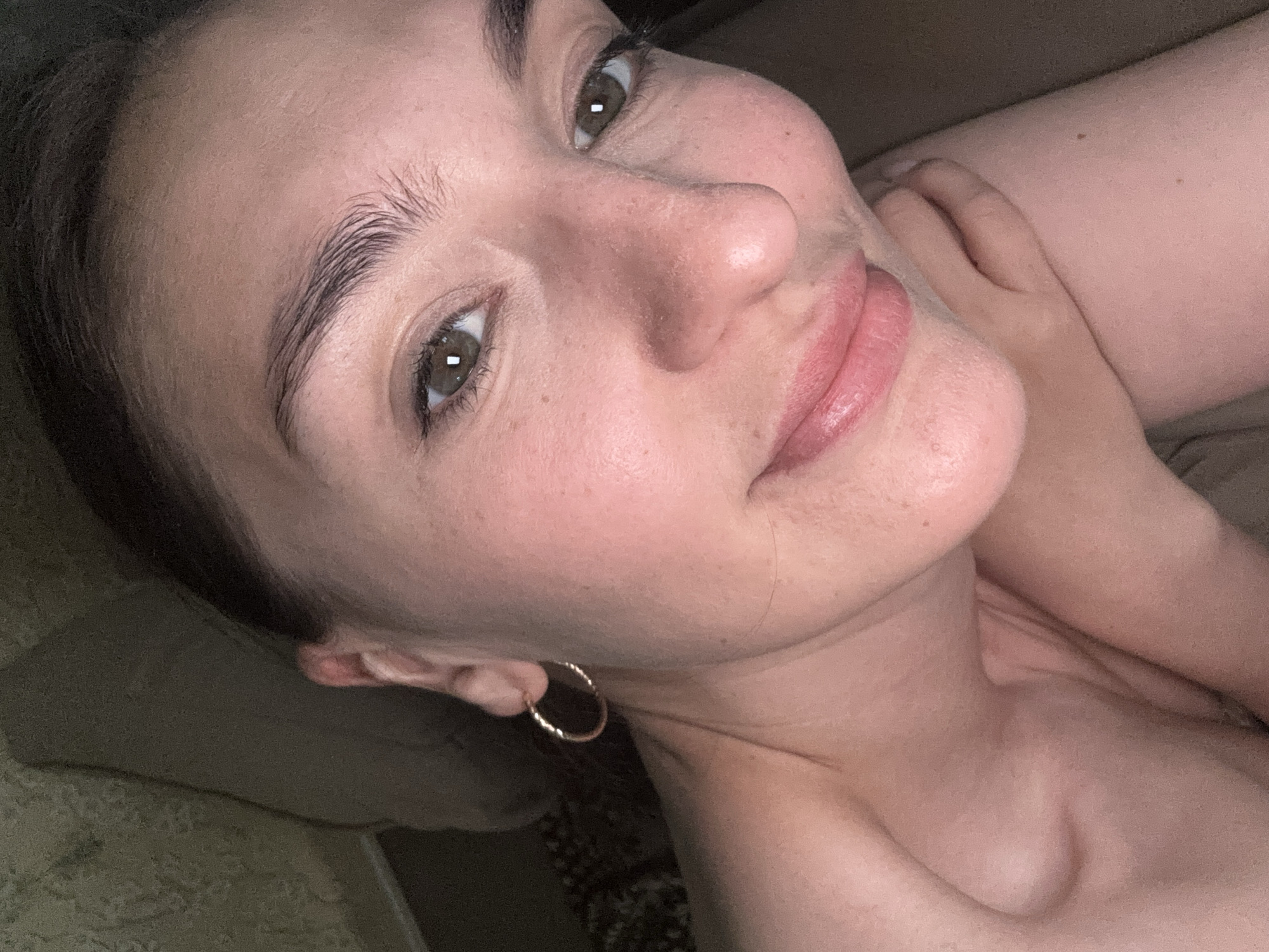 A close-up photograph shows a woman's face. She has fair skin, brown hair, and brown eyes. She is wearing a gold hoop earring. The background is blurred, but appears to be furniture. There is no indication of a location in the city of Sochi, Russia, or any other location.