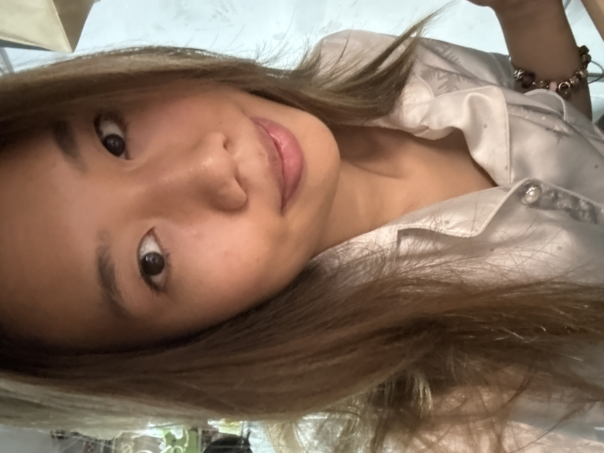A woman with tan skin and brown hair is wearing a white patterned button-up shirt. She is looking towards the camera with a slight smile. A bracelet is visible on her left wrist. No information about Nan'an District, China is discernible in the image.