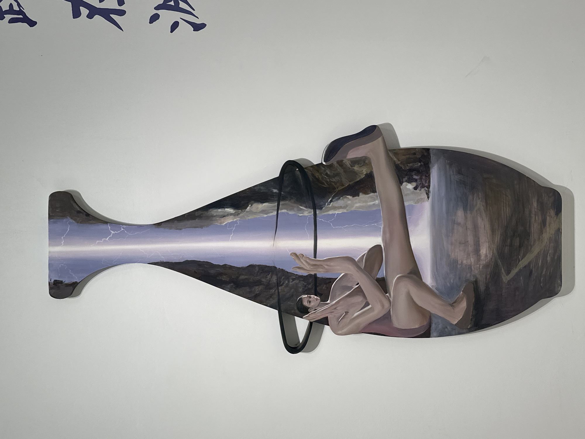 A unique, vessel-shaped artwork is mounted on a white wall. The artwork depicts a reclining nude figure inside what appears to be an amphora or a similar storage container. The container's interior is painted with contrasting scenes: one side features a stormy landscape with lightning and mountains, while the other suggests a dark, possibly watery environment with hints of a waterfall. The figure's limbs are extended, conveying a sense of vulnerability. The vessel has a decorative handle. The image suggests the artwork is located in Banan, China based on Chinese characters on the wall.