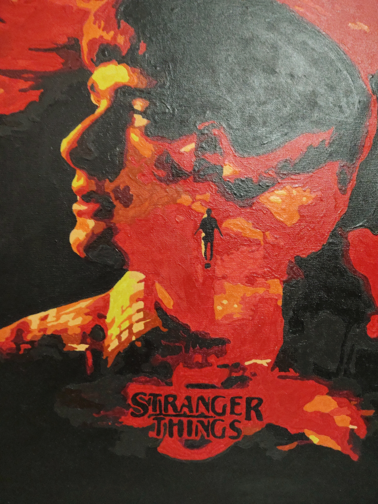 A painting depicts the profile of a person's head, executed in shades of red, orange, yellow, and black. The head is oriented to the left, with the facial features suggested by the color gradations. Within the red area of the neck and jawline, there is a small, silhouetted figure of a person standing. Below the head, in the lower portion of the painting, the words "STRANGER THINGS" are written in a red, stylized font. The background is primarily black.
