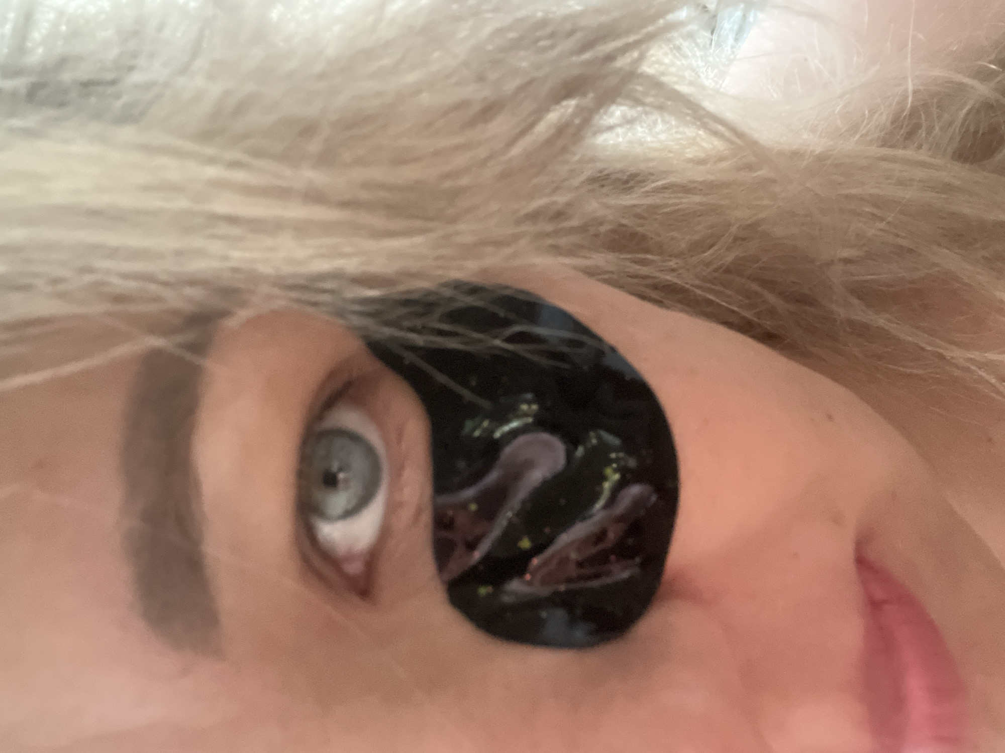 A close-up, tilted image shows a fair-skinned individual with blond or graying hair. Their left eye, which is blue-gray, is visible along with a brow that appears to be filled in with makeup. Underneath the eye, on the cheek area, a black, gel-like eye mask is applied. The lower portion of the nose and part of the upper lip are also visible.
There is no information in the image to identify the location as Chaikovsky, Russia.
