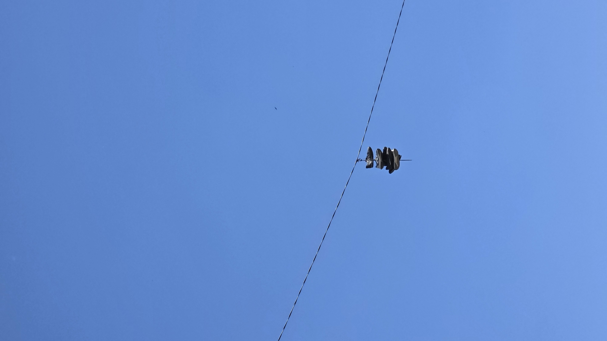 A pair of black sneakers hang from a power line against a clear blue sky. The location is Blagoevgrad, Bulgaria.