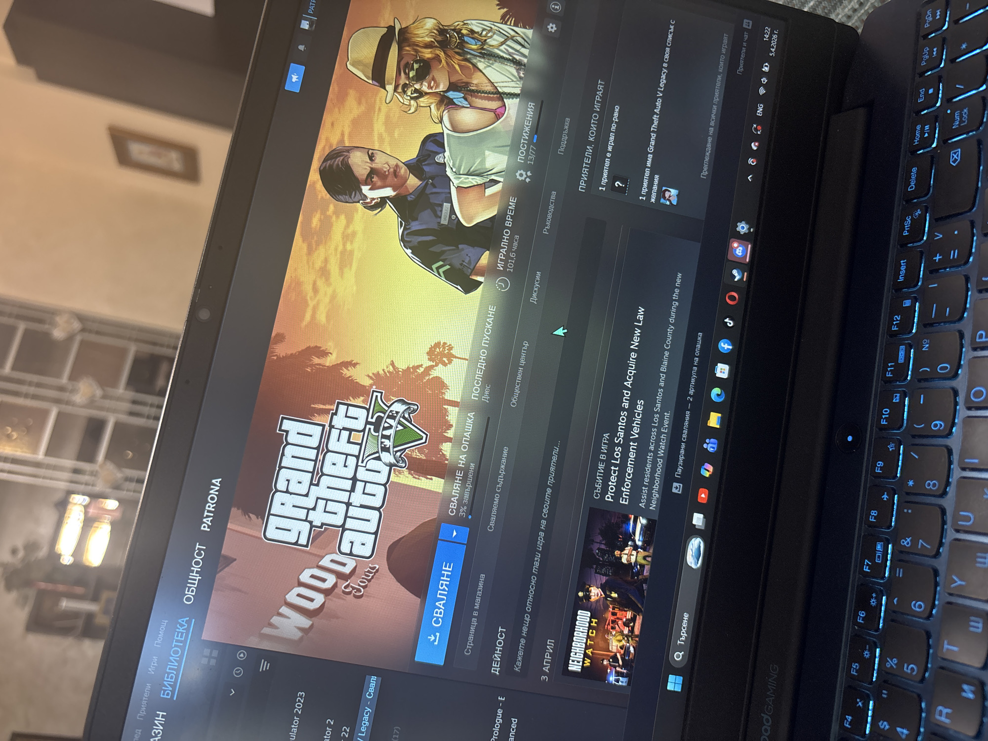 Here's a detailed description of the image:
**Subject:** The image shows a laptop screen displaying the Steam client, specifically the page for Grand Theft Auto V.
**Objects:**
* Laptop: A black gaming laptop is the main object, showing its keyboard in the lower right.
* Steam Client: The software application is open, featuring the GTA V game page. Details like gameplay time (101.6 hours), achievements, and download progress are visible.
* Game Artwork: The GTA V cover art is prominently displayed.
* User Interface Elements: Buttons, text, and icons associated with Steam are present.
**Actions/Interactions:**
* The user is likely browsing the Steam client, possibly interacting with the GTA V game page.
* The game is in the process of being downloaded (indicated by the download progress bar).
* The steam client has a Bulgarian language interface.
**Environment:**
* The image is indoors, with the laptop resting on a textured surface (possibly fabric).
* The lighting is mixed, with some areas appearing brighter due to reflections on the screen.
* There is a slightly out-of-focus picture frame on the wall in the background.
**Location:** The image is on a laptop, but there is no information that indicates the city of Plovdiv, Bulgaria.