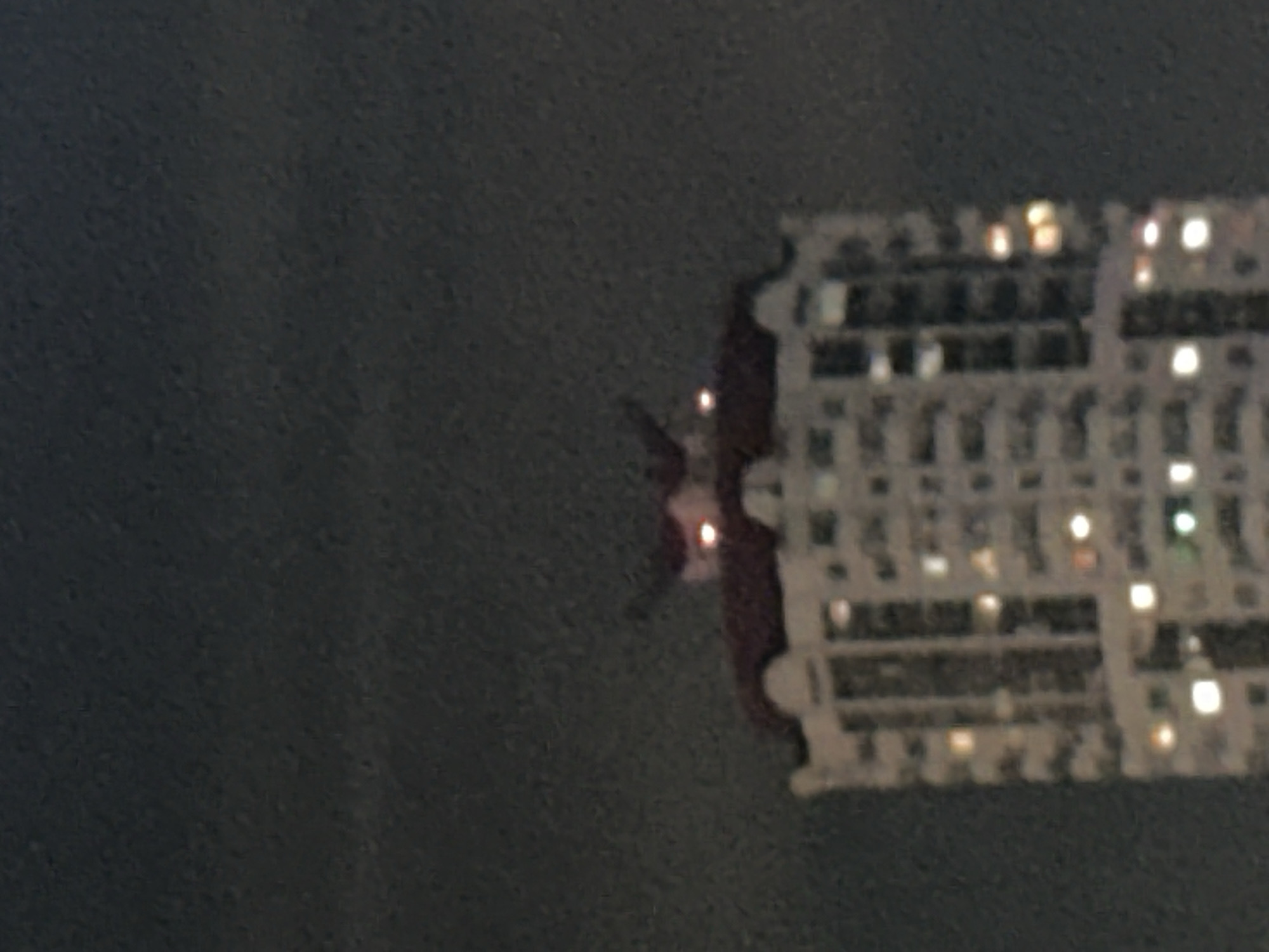 The image shows a blurred view of the lights of a tall building, possibly an apartment complex, reflected in a window at night. The lights are arranged in a grid-like pattern, typical of buildings with many windows. The reflection suggests the image was taken from inside another building or a vehicle. The lack of clarity makes it difficult to determine the exact location in Moscow, Russia, or any specific people or interactions.