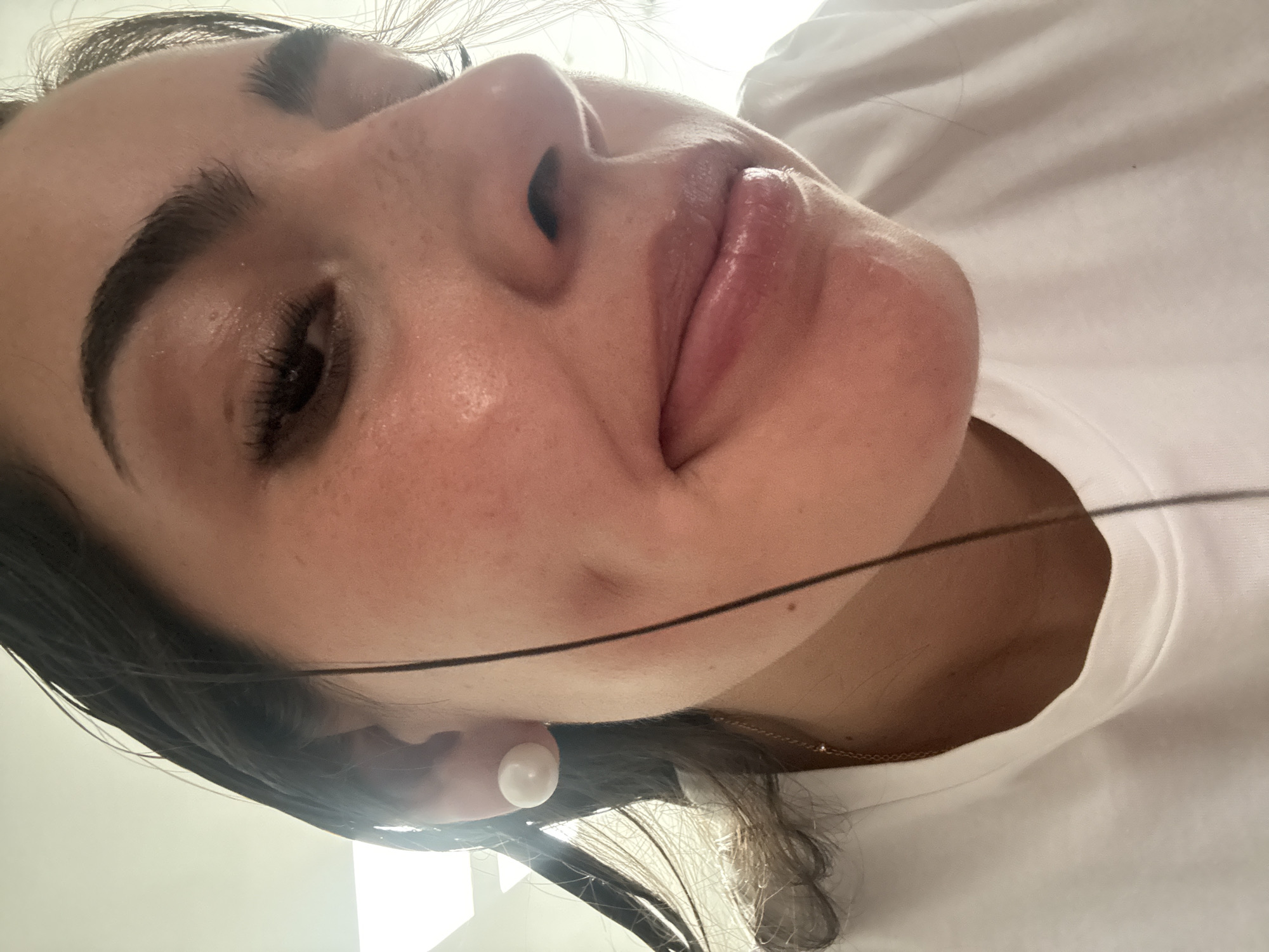 A close-up photograph depicts a woman's face from a low angle. The woman has dark hair, prominent eyebrows, and full lips. She wears a white t-shirt and a white earring. No additional information indicates the location is in San Bernardino Tlaxcalancingo, Mexico.