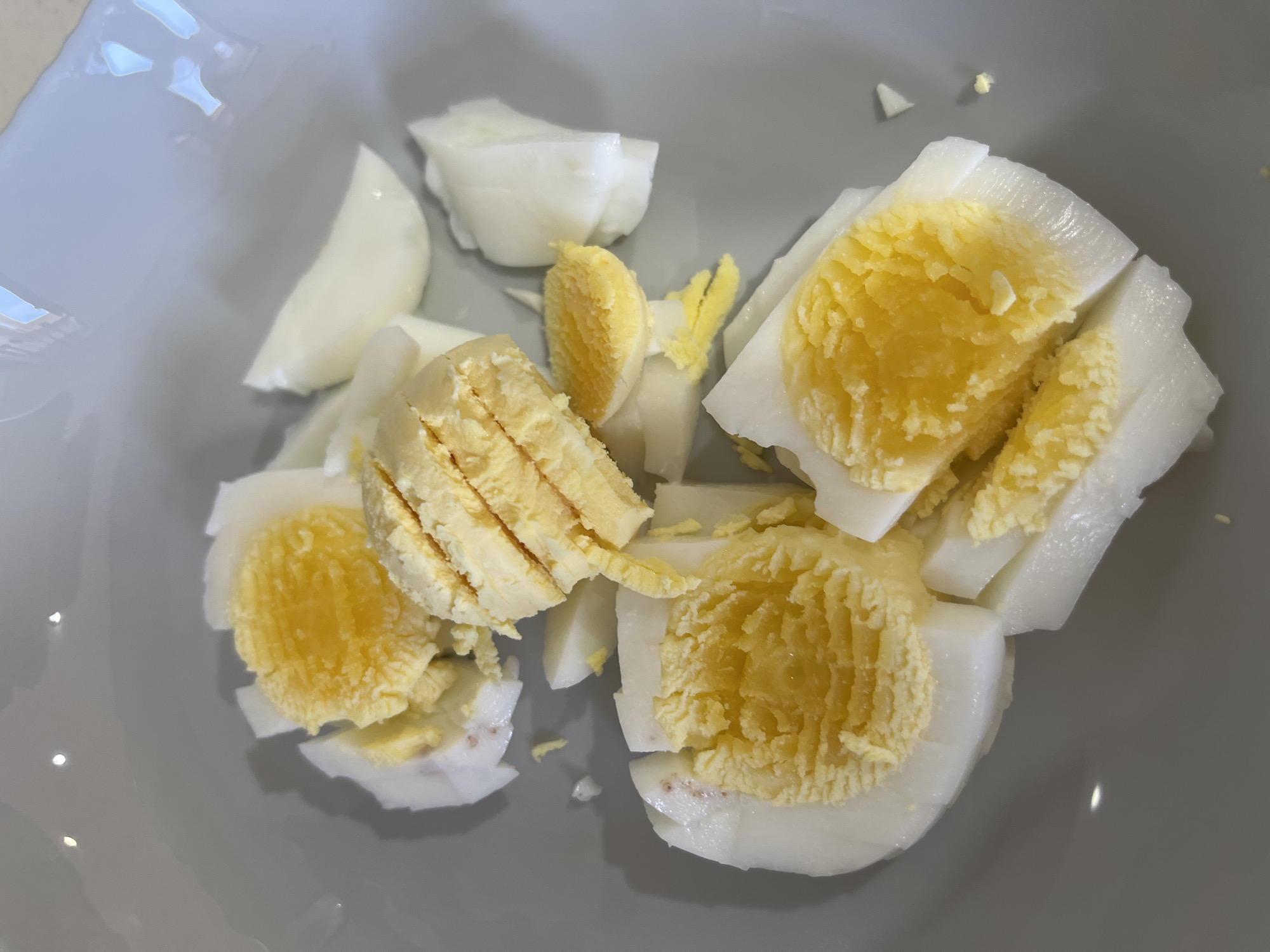 A gray bowl contains chopped hard-boiled eggs. The eggs are sliced and quartered, displaying the white and yellow sections. The bowl rests on a light-colored surface. The image was not taken in Chaikovsky, Russia, and no people, subjects, or actions can be identified.