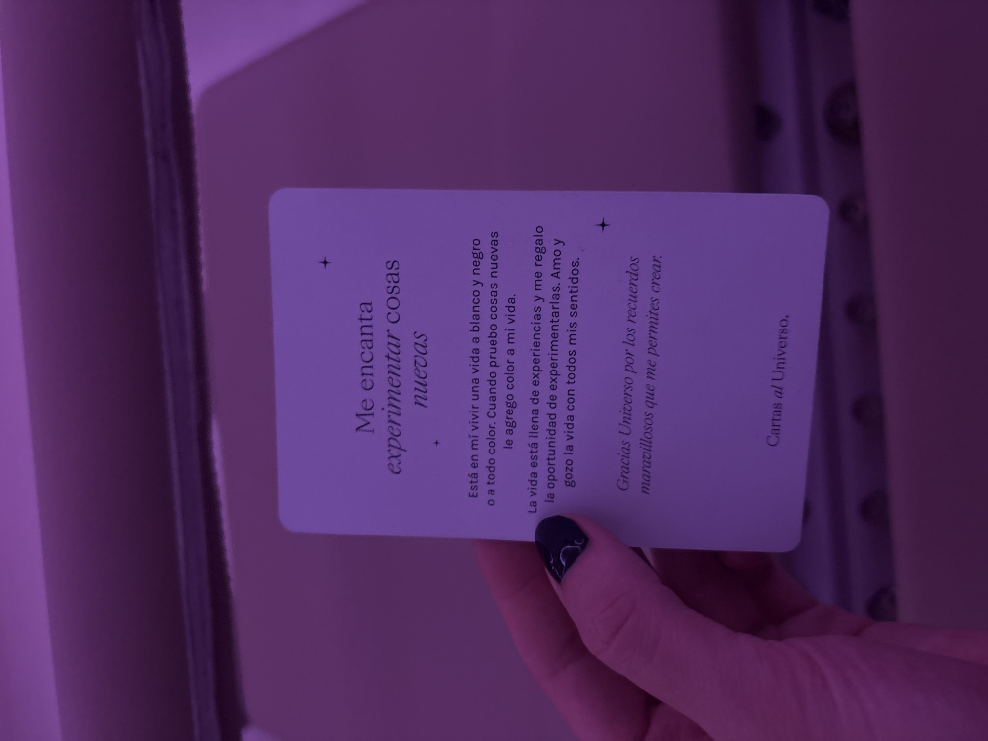 The image shows a hand holding a card from "Cartas al Universo" (Letters to the Universe). The card has the following text in Spanish: "Me encanta experimentar cosas nuevas. Está en mí vivir una vida a blanco y negro o a todo color. Cuando pruebo cosas nuevas le agrego color a mi vida. La vida está llena de experiencias y me regalo la oportunidad de experimentarlas. Amo y gozo la vida con todos mis sentidos. Gracias Universo por los recuerdos maravillosos que me permites crear." This translates to: "I love to experience new things. It's up to me to live a life in black and white or in full color. When I try new things, I add color to my life. Life is full of experiences and I give myself the opportunity to experience them. I love and enjoy life with all my senses. Thank you Universe for the wonderful memories you allow me to create." The image does not show the location in the city of Mexico City, Mexico.