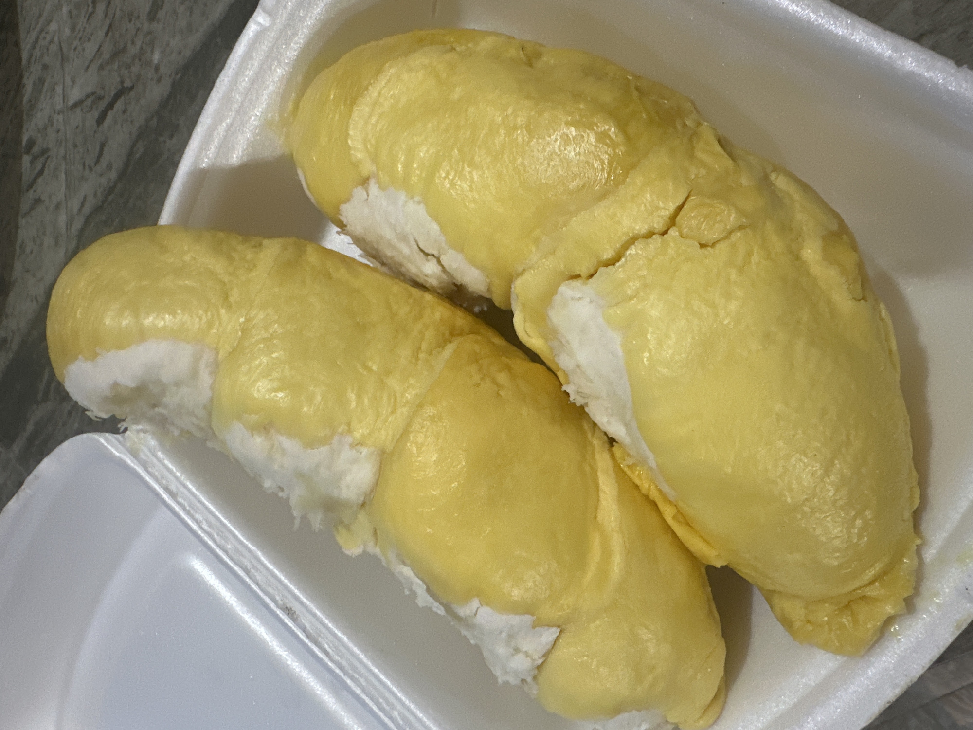 The image shows two portions of durian fruit in a white styrofoam container. The durian flesh is pale yellow in color and has a characteristic segmented shape. The fruit rests on a white, fibrous base, likely the fruit's husk interior. The container sits on a surface with a grey marbled pattern. The location of Bac Nha Trang Ward, Vietnam is not apparent from the image.