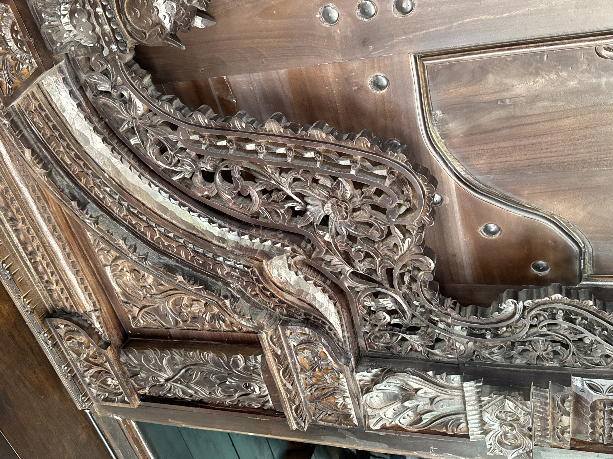 Detailed view of intricately carved dark brown wooden panels, likely part of a door or furniture, showcasing detailed floral and geometric patterns. The location is in Ungasan, Indonesia, as inferred from the style of woodwork which is common in the region. The image focuses on the elaborate craftsmanship and rich texture of the carved wood.