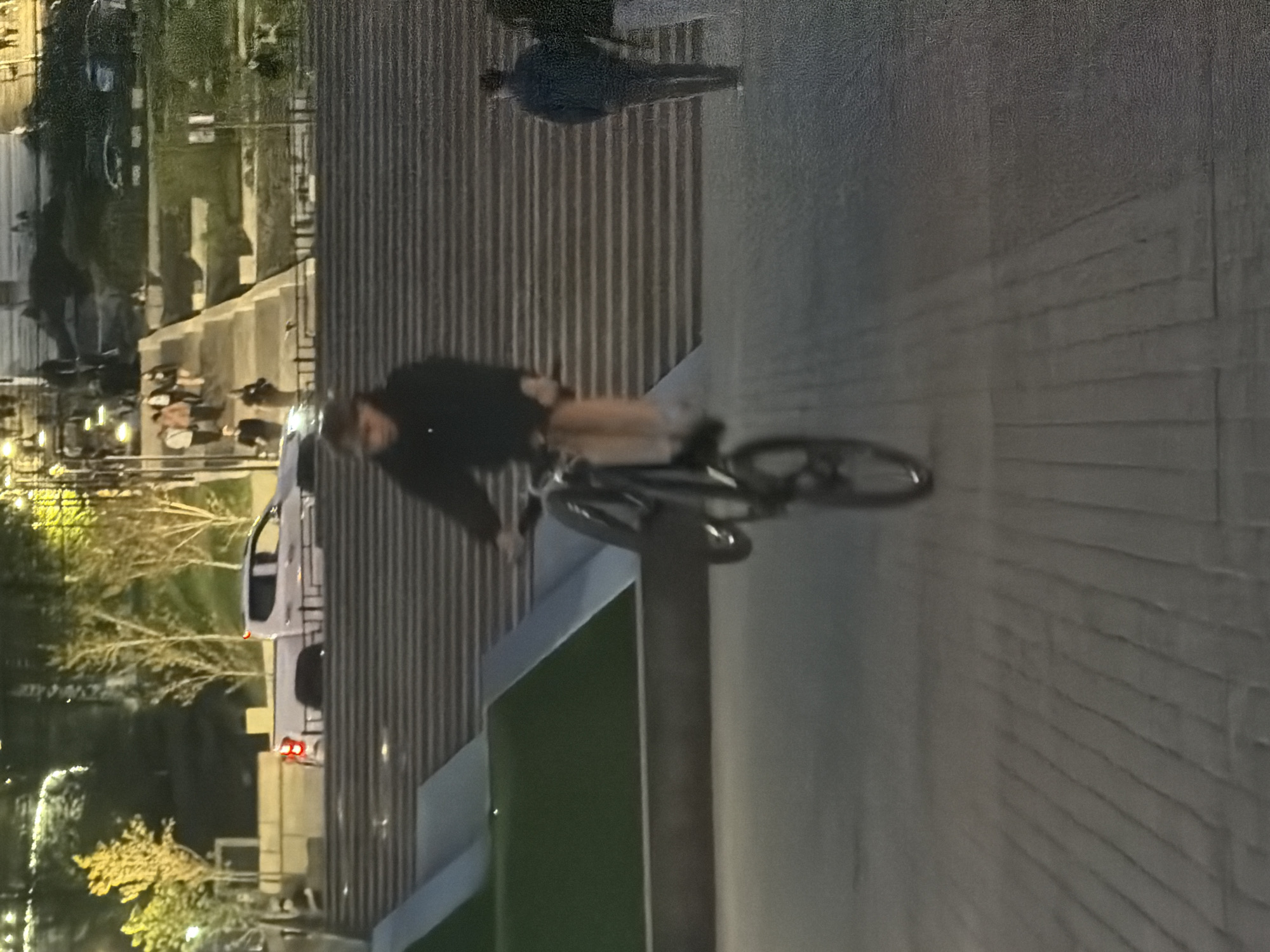 The image shows a cyclist on a bicycle riding on a paved surface. In the background, there are steps, and further back, trees and buildings. There is also a person standing near the steps. The location is Izhevsk, Russia.