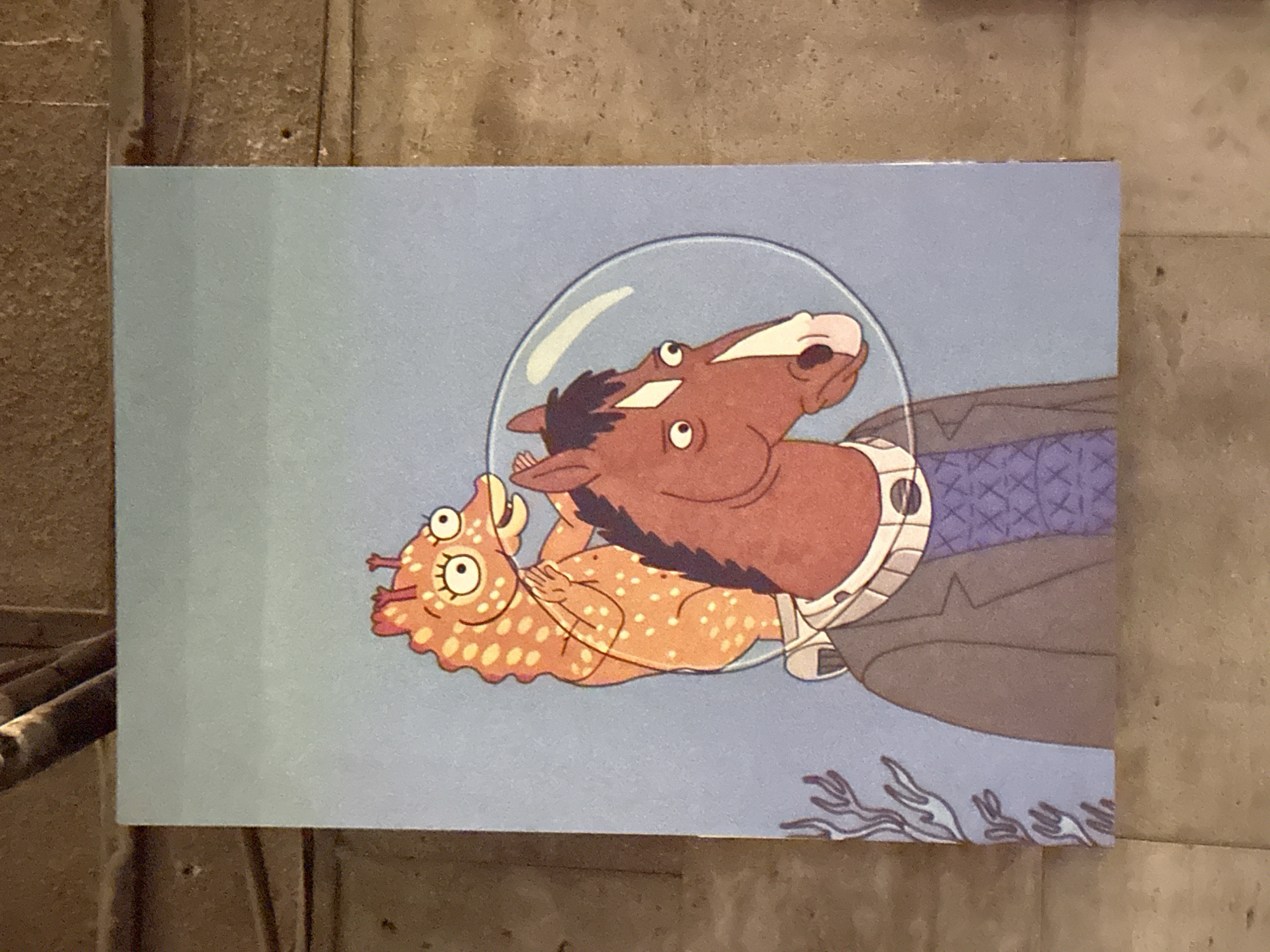 The image shows a rectangular postcard or print on a textured, light-colored surface. The postcard features an illustration of BoJack Horseman and Princess Carolyn from the animated show "BoJack Horseman". They are depicted wearing spacesuits. BoJack is shown as a horse, and Princess Carolyn is shown as a cat-like creature. The background is a blue color, suggesting they are underwater. There is no indication of the location of the image in Yerevan, Armenia.