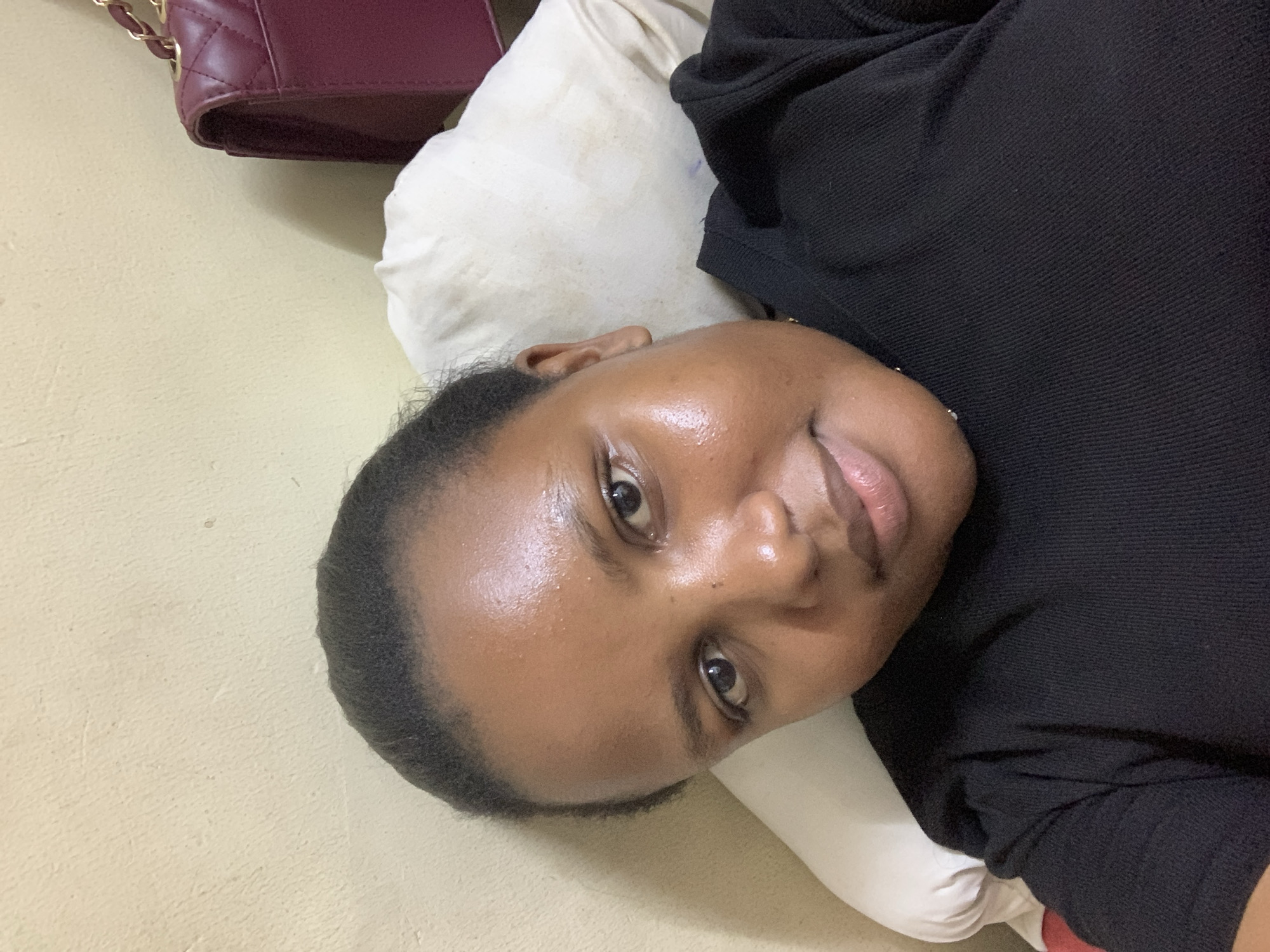 The image depicts a person lying on a pillow, wearing a black top. A burgundy purse is positioned near the top left corner. The location is suggested to be Dar es-Salaam, Tanzania.