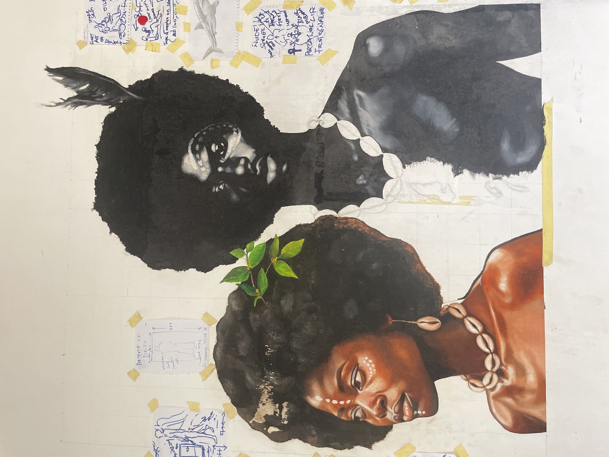 The image depicts a work in progress, likely an oil painting, featuring two portraits of individuals with dark hair and skin. The lower portrait is largely complete and shows a person with warm skin tones, wearing a shell necklace and green leaves in their hair. Their face is turned to the side with eyes closed. The upper portrait is less complete, rendered in black and white, with less detail. The person also wears a shell necklace, and a feather adorns their hair. Both figures are oriented in a horizontal position.
The background is a white surface marked with a grid of faint lines, possibly a canvas or drawing board. Attached to the background with yellow tape are several small notes or sketches, some containing writing and diagrams. A diagram depicting a figure, possibly in the city of Ado, Nigeria, is among these notes.