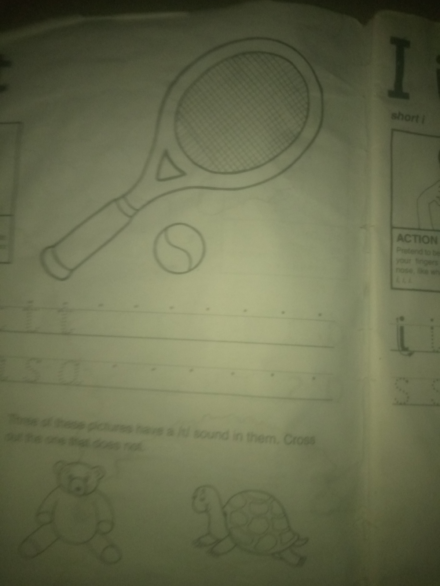The image displays a page from a children's workbook with handwritten and printed text and illustrations. In the upper left quadrant, a drawing of a tennis racket and ball is visible. Below this, there are dotted lines for handwriting practice. In the lower half of the page, there are drawings of a teddy bear and a turtle, accompanied by text that appears to be an instruction related to identifying sounds in pictures. On the right side of the page, there are large letter "I" and "i" characters, along with printed text and an illustration of a hand near a nose. The background appears to be a plain surface, possibly a table or a desk, and the lighting suggests an indoor environment. The image is a close-up, focused on the workbook content. The location of Jauro Yinu, Nigeria is not depicted or suggested in the image.