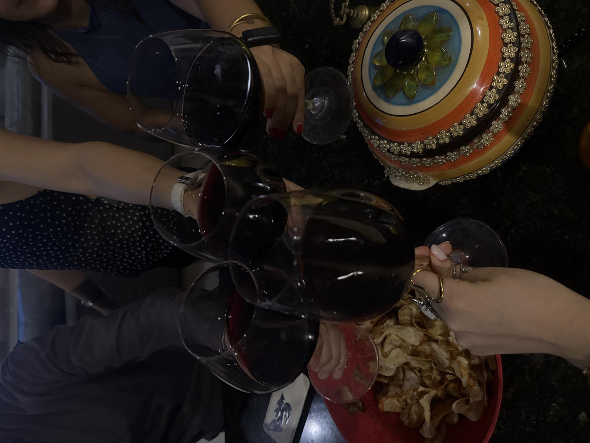Four people are raising glasses of red wine for a toast. A decorative lidded bowl sits nearby. A bowl of potato chips is visible next to one of the wine glasses. The location is Santa Clara Ocoyucan, Mexico.