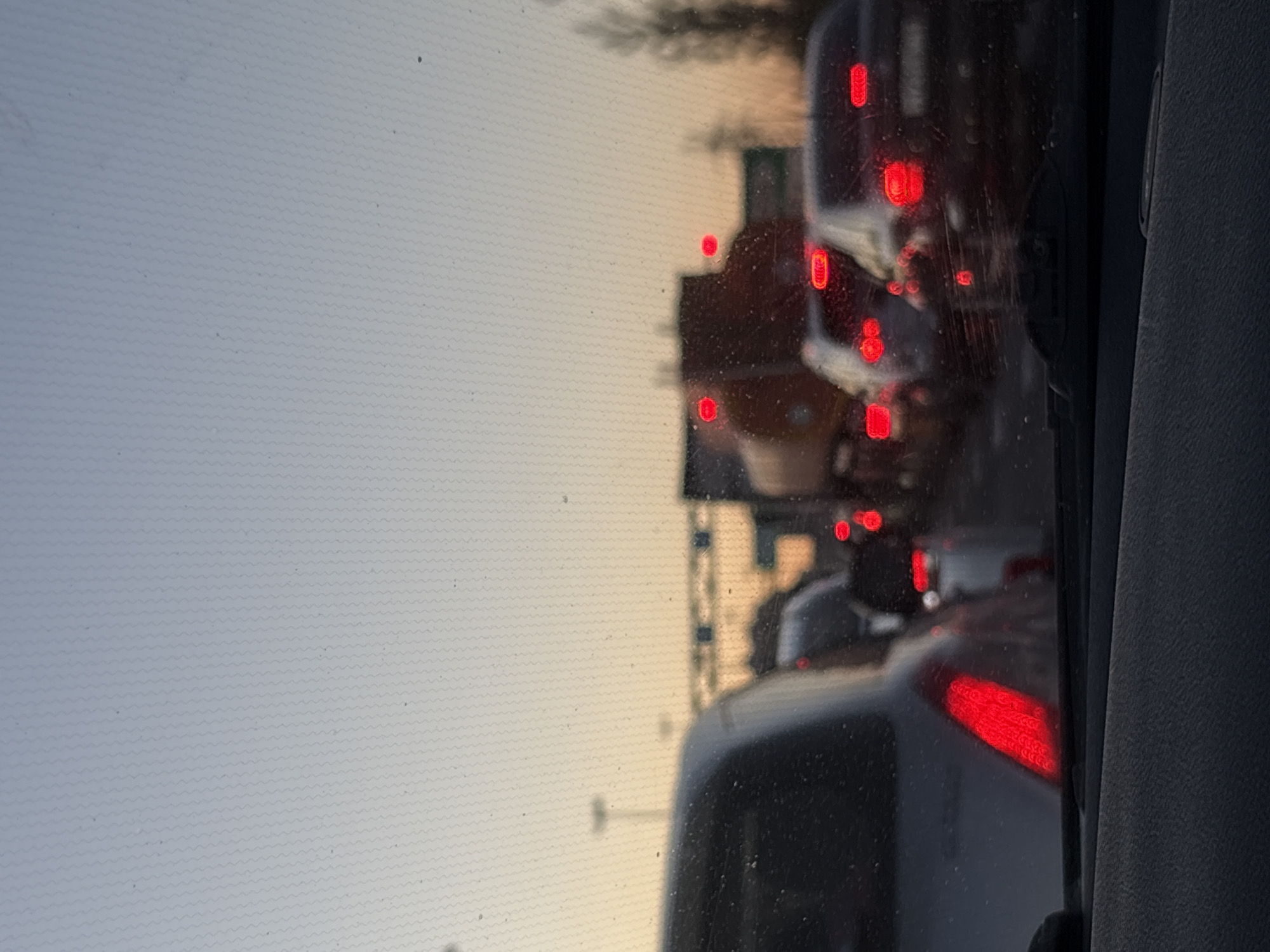 The image shows a view from inside a car, looking out at traffic congestion. Multiple vehicles are visible ahead, indicated by their red taillights. The sky is pale and overcast. The location is in an urban environment, characterized by cars, traffic lights, and possibly buildings. The city and country are specified as Unknown, Russia.