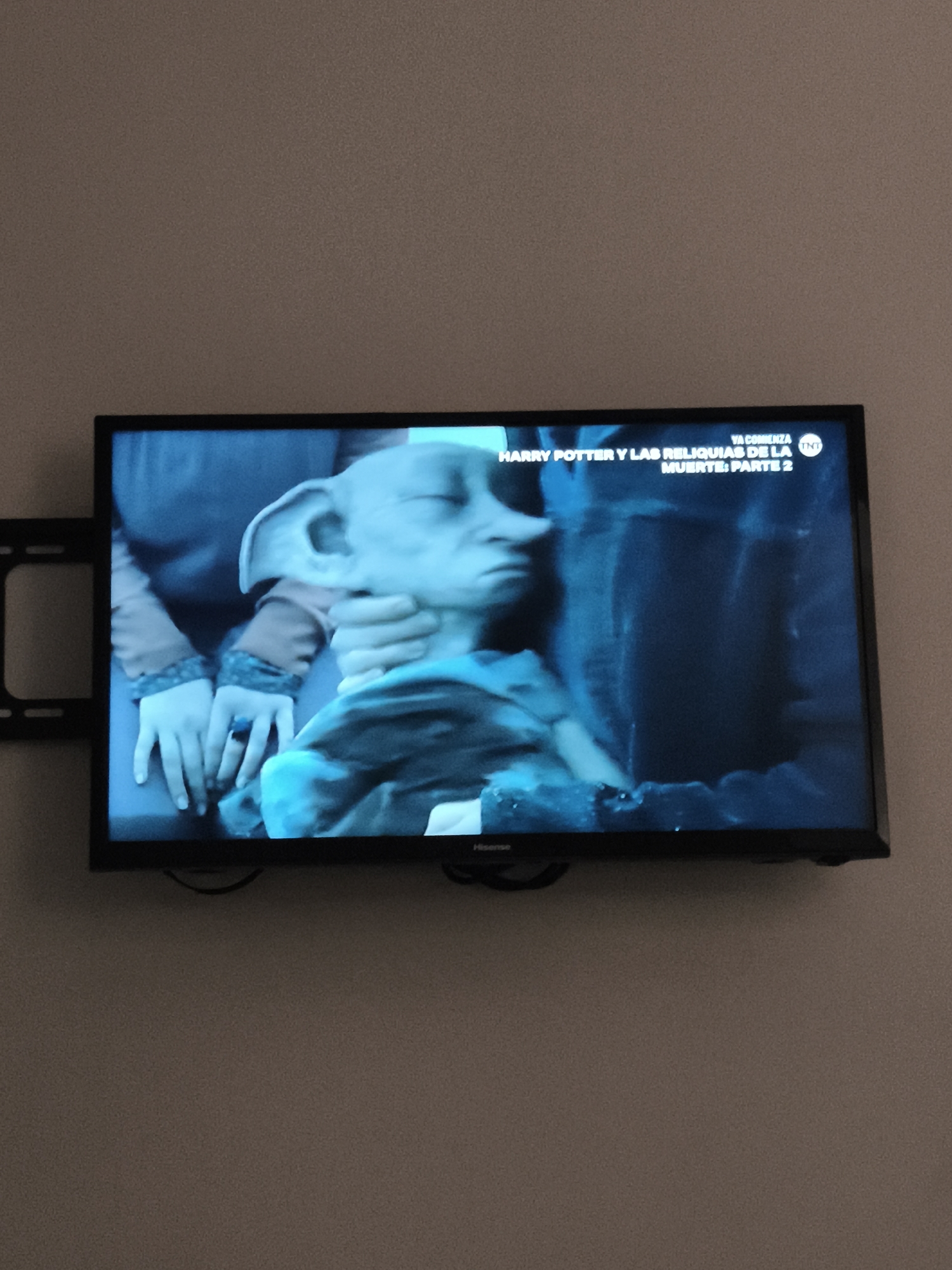 A television mounted on a wall displays a scene from "Harry Potter y las Reliquias de la Muerte: Parte 2." The scene features a character resembling Dobby, the house-elf, being held. The TV is a Hisense brand. The setting is unknown, but the location is Guatemala City, Guatemala.
