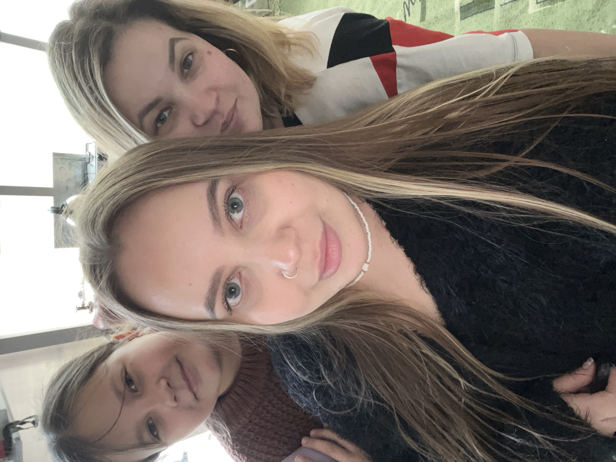 Three people are in the image. A young girl is in the lower left of the image. An adult woman with long hair and a nose ring is in the middle. Another adult woman is in the upper part of the image. The location is not discernable.