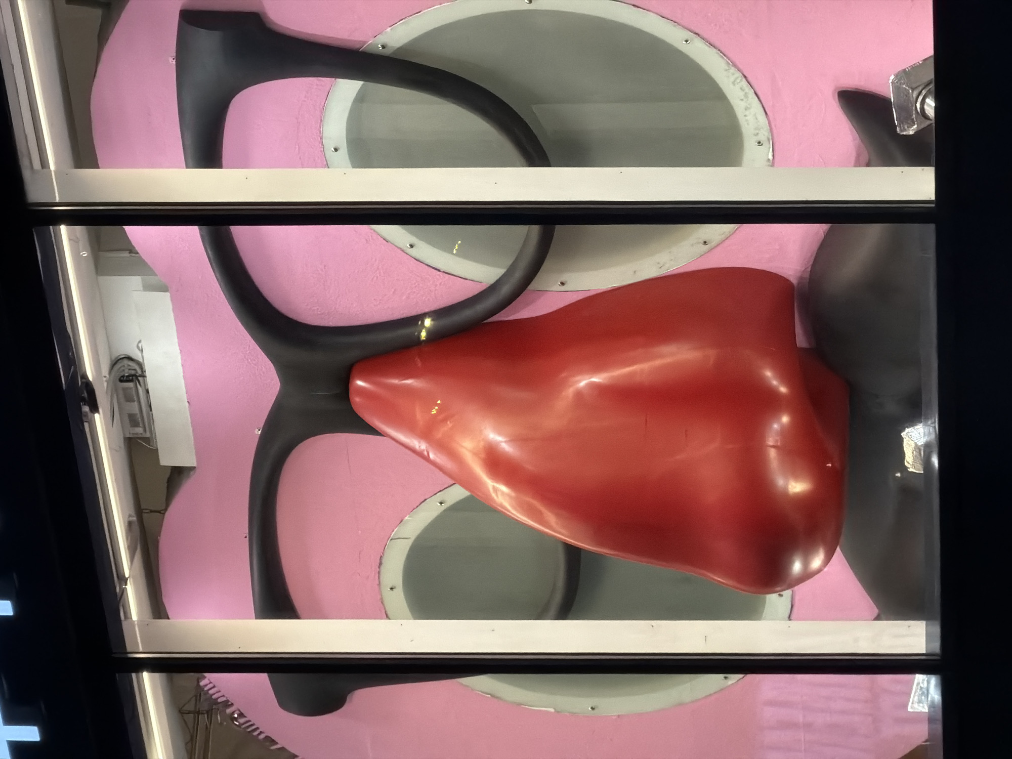 A view through a window shows a large, stylized, pink cartoon character. The character has large black-rimmed glasses, a prominent red nose, and visible nostrils. The pink skin appears textured. Circular grey vents are visible on the character's face. The window has a white frame. The scene is likely within the city of Moscow, Russia.