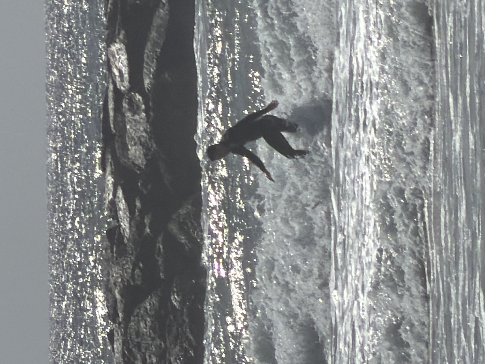 A person in dark clothing is falling or diving off a dark cliff or ledge into a body of water that appears to be a waterfall or rapidly flowing river. The water reflects sunlight. There is no visible evidence to suggest the location is Tel-Aviv, Israel.