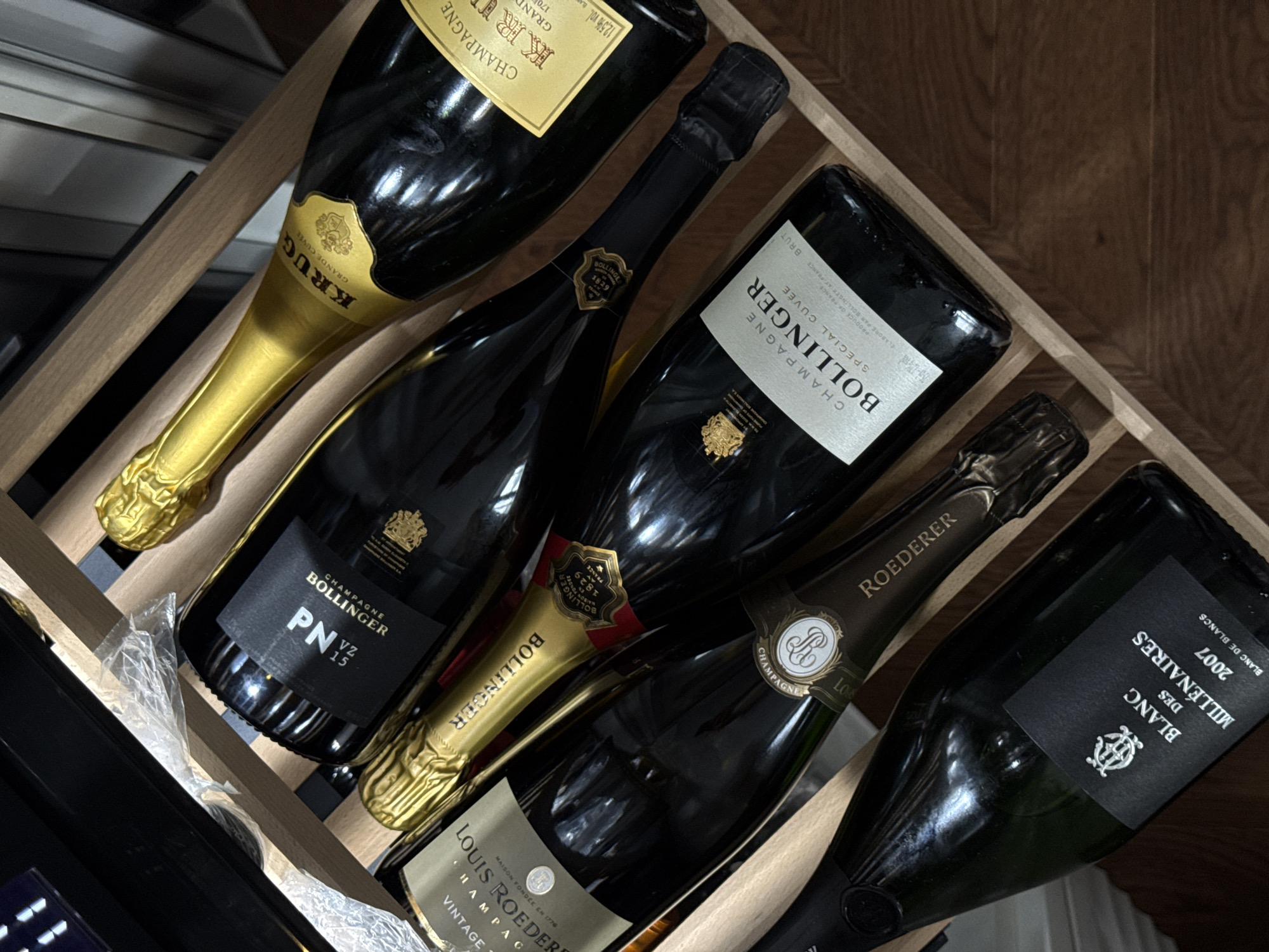 The image shows a wooden wine rack containing several bottles of champagne. Prominent brands include Krug Grande Cuvée, Bollinger (Special Cuvée, PN VZ15), Louis Roederer, and Blanc des Millénaires 2007. No location in Moscow, Russia, is evident in the image.