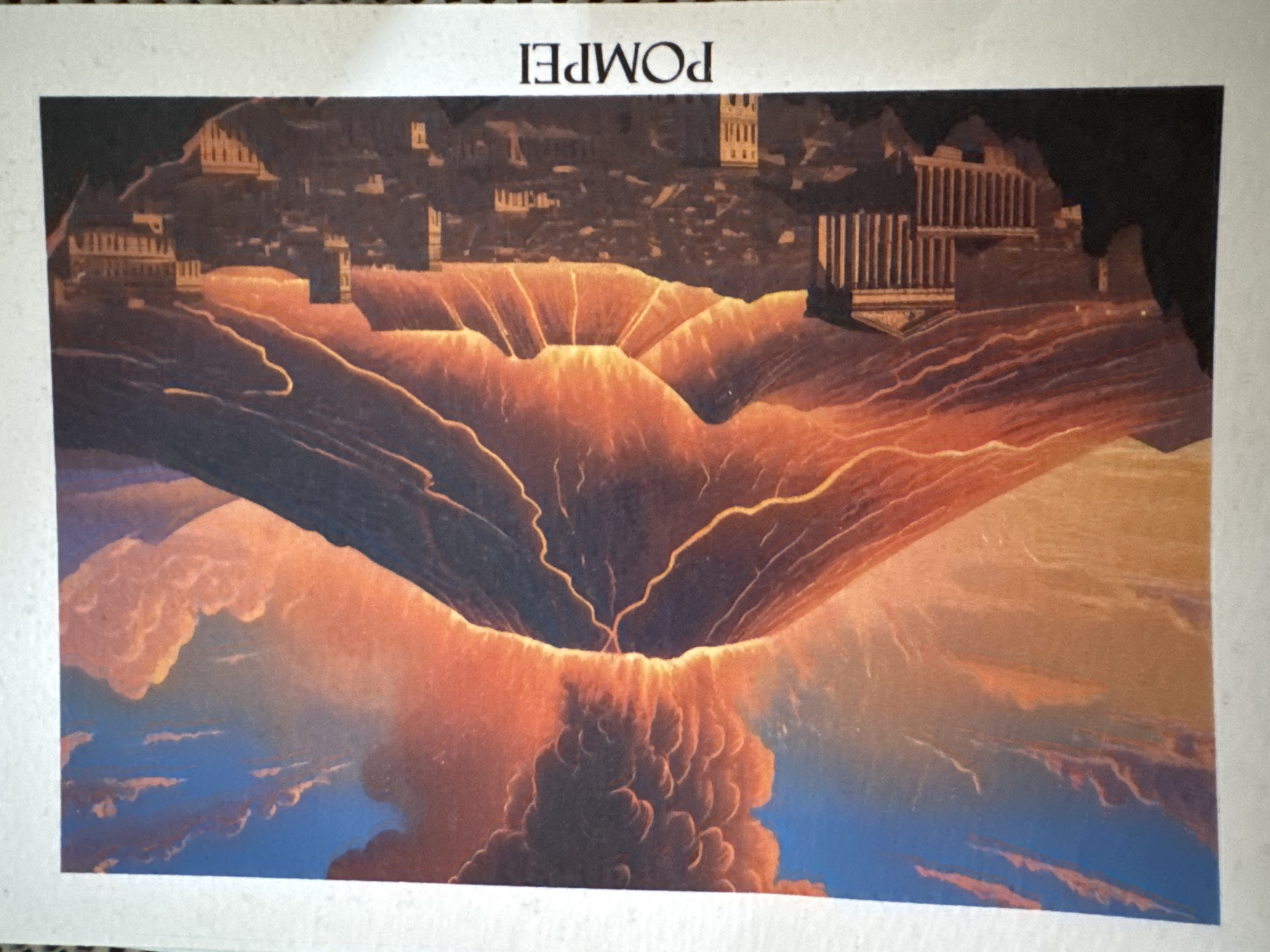 The image depicts a catastrophic volcanic eruption of Mount Vesuvius engulfing the ancient Roman city of Pompeii. In the background, the city's buildings, including temples and structures with columns, are visible as silhouettes. A massive, orange and red cloud of ash and pyroclastic flow descends from the volcano's crater, appearing to consume the city. The foreground shows a mix of orange, red, and blue, suggesting ash clouds mixing with the sky. The city of Sofia, Bulgaria, is NOT depicted in this image.