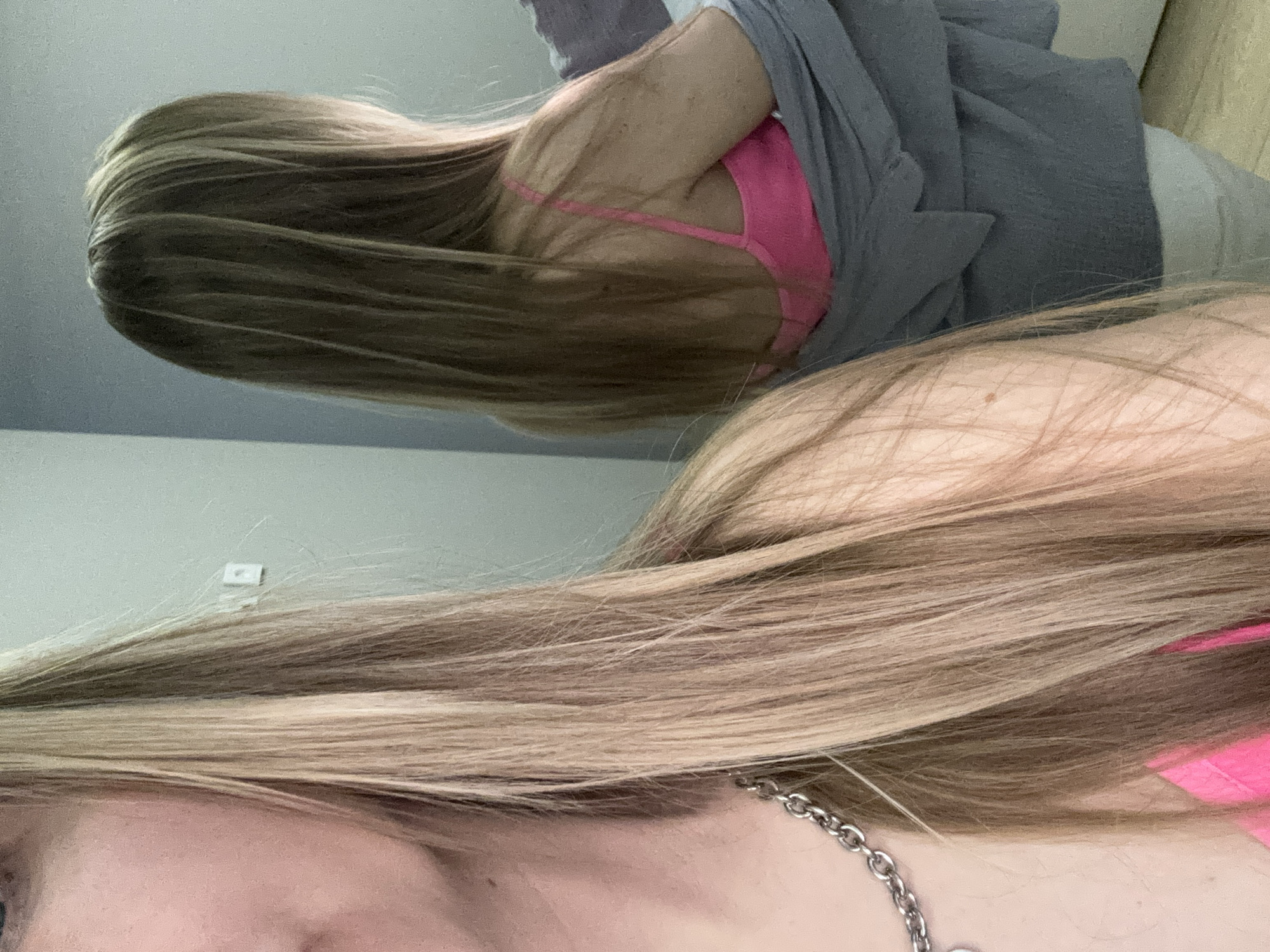 The image shows two individuals, possibly women, with blonde hair. One is wearing a pink top and a silver necklace. The other is wearing a pink top underneath a gray garment. The background suggests an indoor setting with a light blue wall. There is no information in the image to suggest a location in Chaikovsky, Russia.
