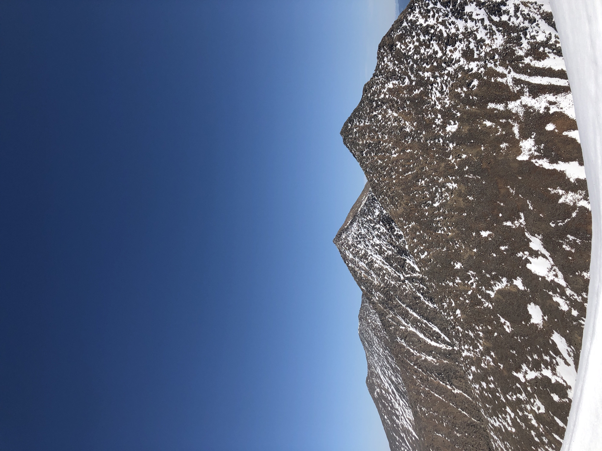 The image shows two mountains with snow and a blue sky. The mountains are brown with patches of white snow, and the sky is a clear, deep blue.