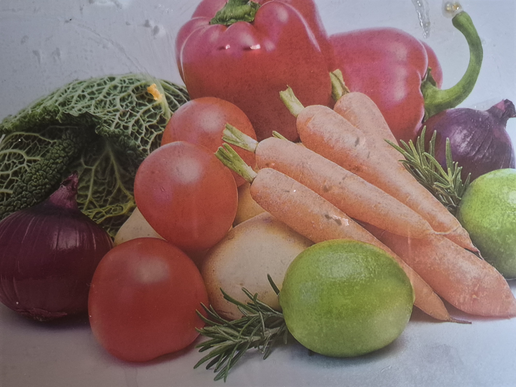 This close-up, high-angle still life image presents a vibrant array of fresh vegetables and fruits, artfully arranged on a light-colored, possibly textured, surface. The composition features a rich palette of reds, oranges, greens, and purples.
Prominently displayed are several large, glossy red bell peppers, one with a distinctive green, curled stem pointing upwards, and numerous bright red tomatoes. A large head of savoy cabbage, with its deeply veined and crinkled green leaves, occupies the left side of the frame. Several long, orange carrots are clustered towards the right and center, with some of their green leafy tops still attached. Dark red onions are interspersed throughout the arrangement, providing a contrasting deep hue. Two bright green limes are visible, adding a pop of fresh color. In the background, a lighter-skinned bulb, possibly a potato or a pale onion, is partially visible. Scattered among the produce are sprigs of green rosemary, contributing a textural and aromatic element.
The produce appears fresh and clean, with some items exhibiting subtle reflections or water droplets, suggesting they have just been washed. The lighting is bright and even, highlighting the colors and textures of each item. There are no people, visible activities, or discernible text in the image. The scene is a static depiction of healthy ingredients. The image itself does not provide any visual cues to indicate the location of "Yerevan, Armenia."