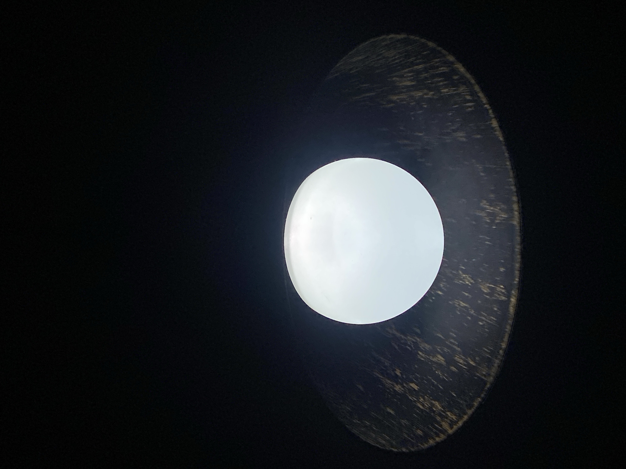 A light bulb is mounted inside a lampshade with a dark finish. The lampshade is partially visible, appearing mainly on the right side of the frame. The light bulb is centrally located, and the rest of the scene is dark. There is no specific context to indicate that the image was taken in Puebla, Mexico. The image does not depict any people, actions, or interactions.