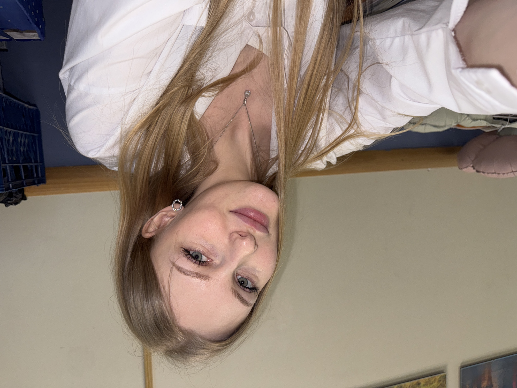 A woman with long blonde hair is seen wearing a white button-down shirt and a necklace. She appears to be indoors. The location is the city of Perm, Russia.