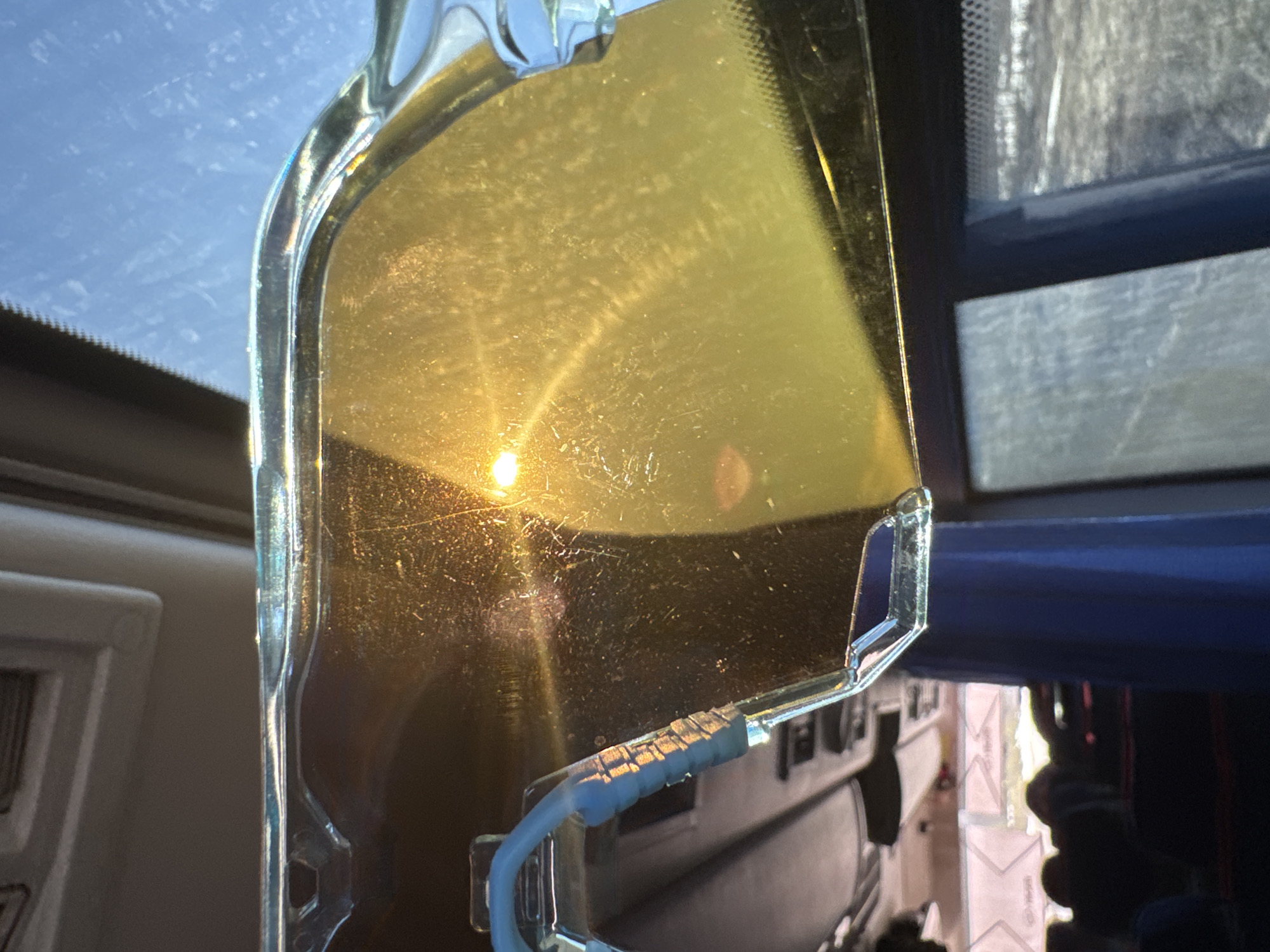 A yellow, rectangular sun visor is positioned in the interior of a vehicle, obscuring a view of the outside. The visor is made of a translucent yellow material with a clear plastic frame. Light reflecting off the visor gives the impression of the sun, though it is not clear if this is the sun or an artificial light source. The interior of the vehicle, including the dashboard, is visible, suggesting a car or truck. The vehicle is presumed to be in the city of Челва, Russia based on the prompt.