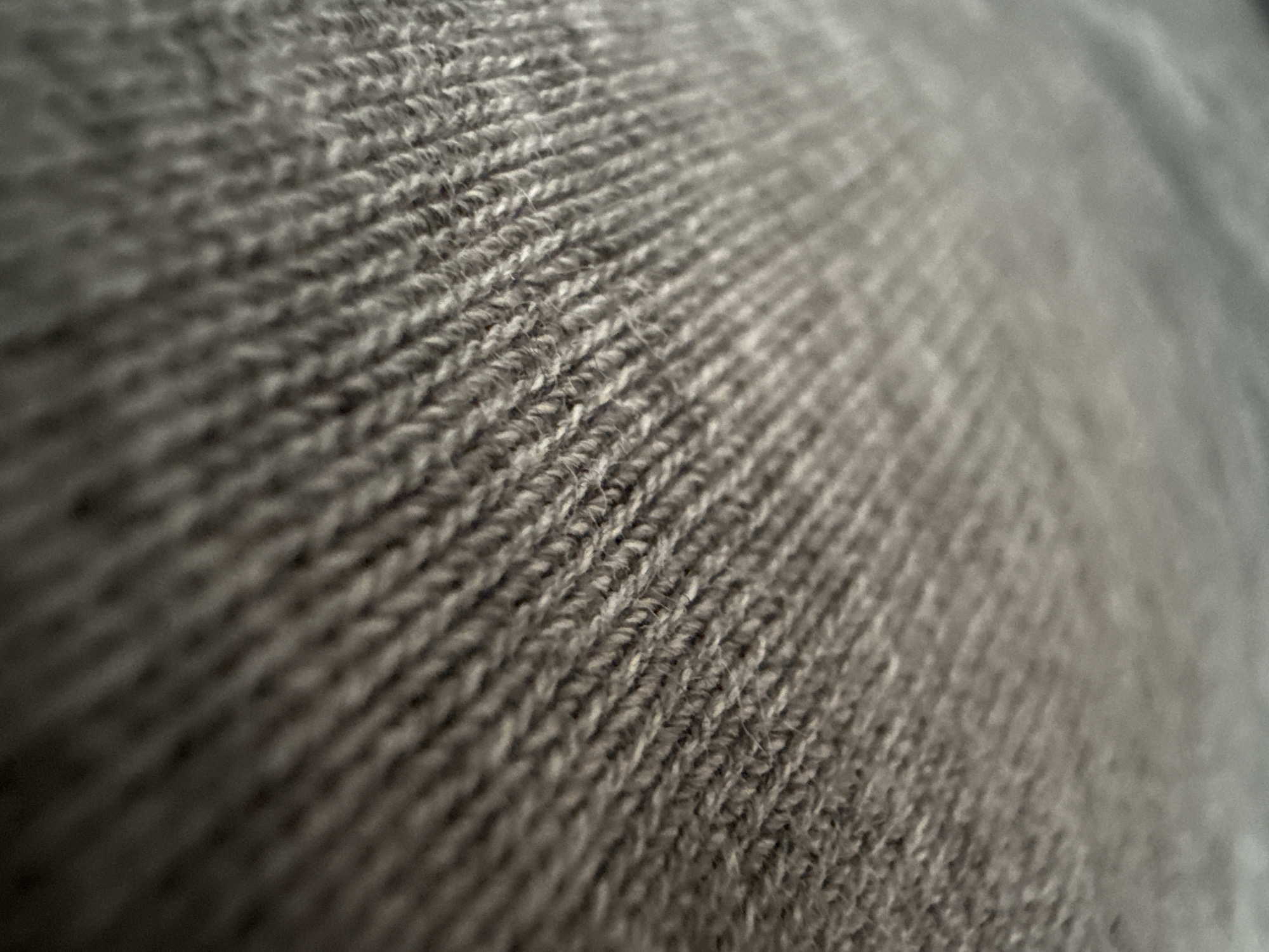 The image shows a close-up view of a gray knitted fabric. The knit pattern is clearly visible, with interlocking loops of yarn creating a textured surface. The fabric is slightly out of focus towards the right side of the frame. There is no information to suggest this image was taken in Lovech, Bulgaria. No people, actions, interactions, or specific environment details are present.