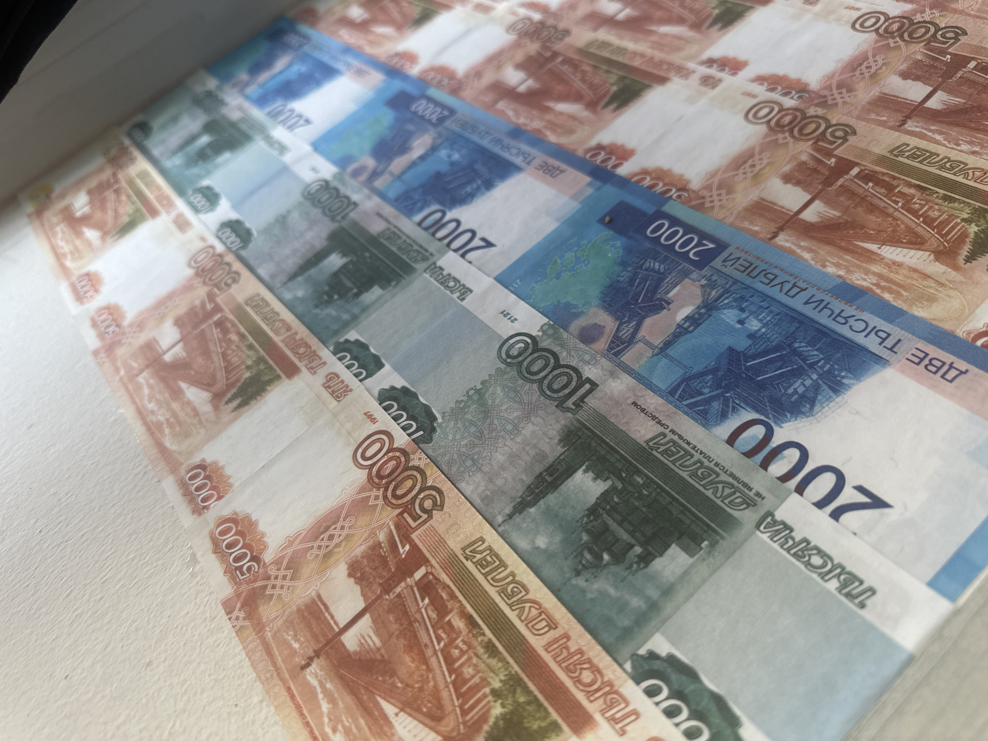 The image shows a close-up of several Russian ruble banknotes arranged in rows on a white surface. The denominations visible are 5000, 1000, and 2000 rubles. The banknotes are slightly angled, creating a perspective effect. The location in the city of Chaikovsky, Russia, is not discernible from the image.