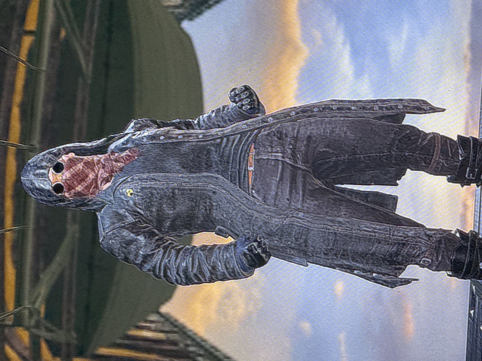 A person stands outdoors, wearing a hooded, dark, long coat over a dark shirt and dark pants. The person's face is obscured by a checkered mask and goggles. The background appears to be a sky with clouds and distant structures, possibly a city or industrial area. The image is captured from a low angle, focusing on the subject. There is no indication of Parma, Italy, or any specific city in the visual information provided.